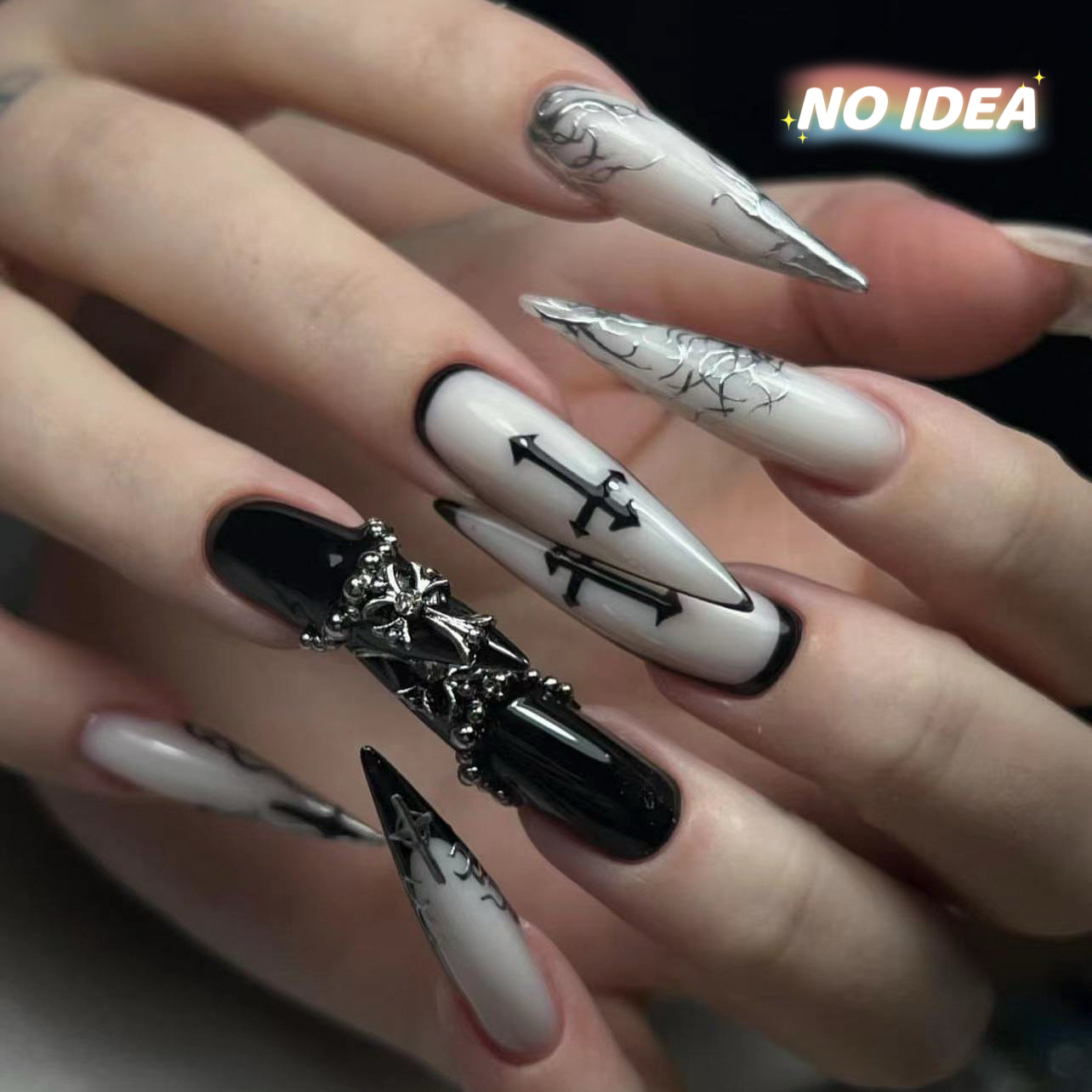 Long almond shaped press on nails in black and white with a prominent silver metal cross decoration.