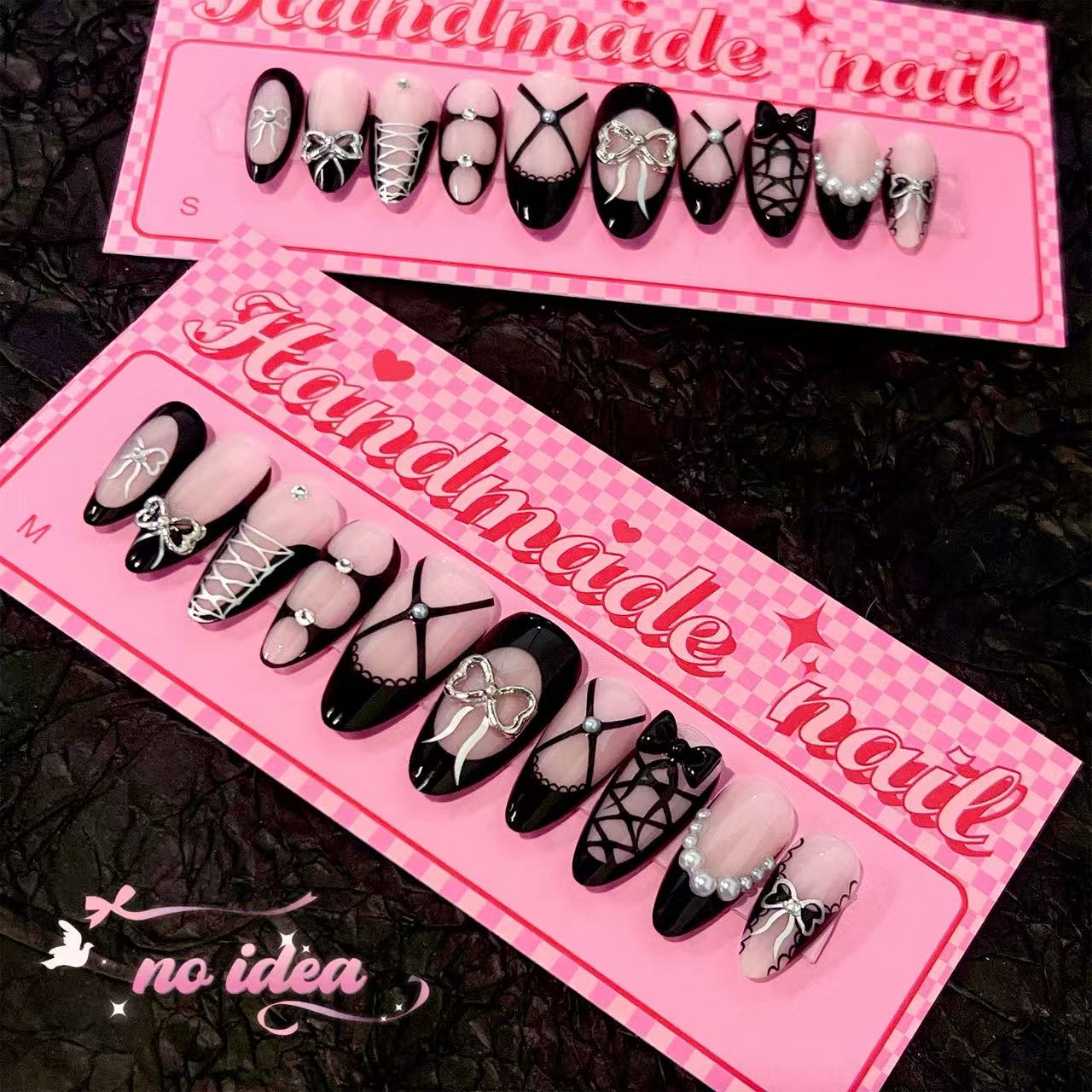 Long almond fake nails in black metallic with a large, reflective 3D silver bow on the ring finger, displayed with glue and tools.