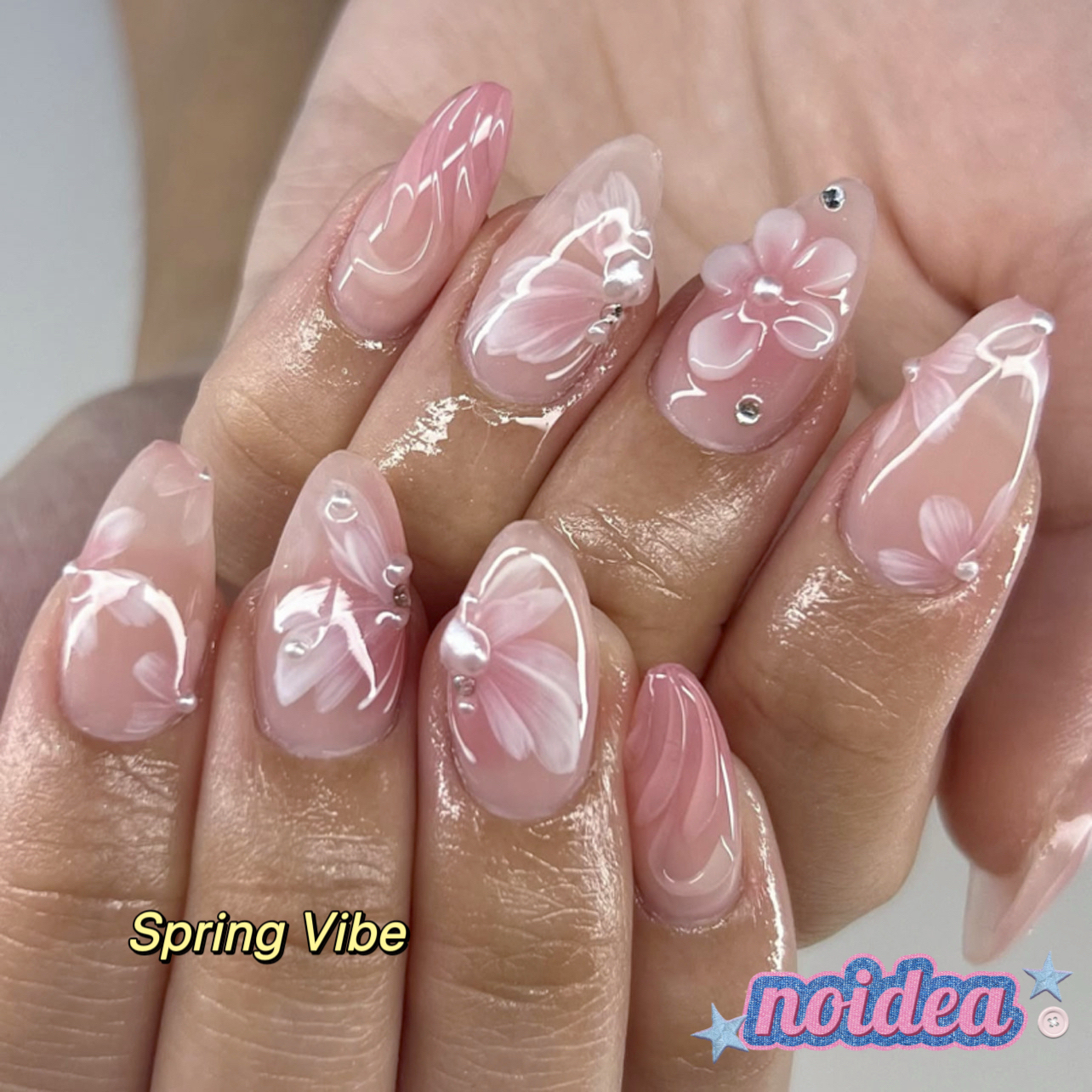 24 pieces of short almond-shaped press on nails with pink and white floral design, shown with jelly glue and tool, laid out to display 12 sizes