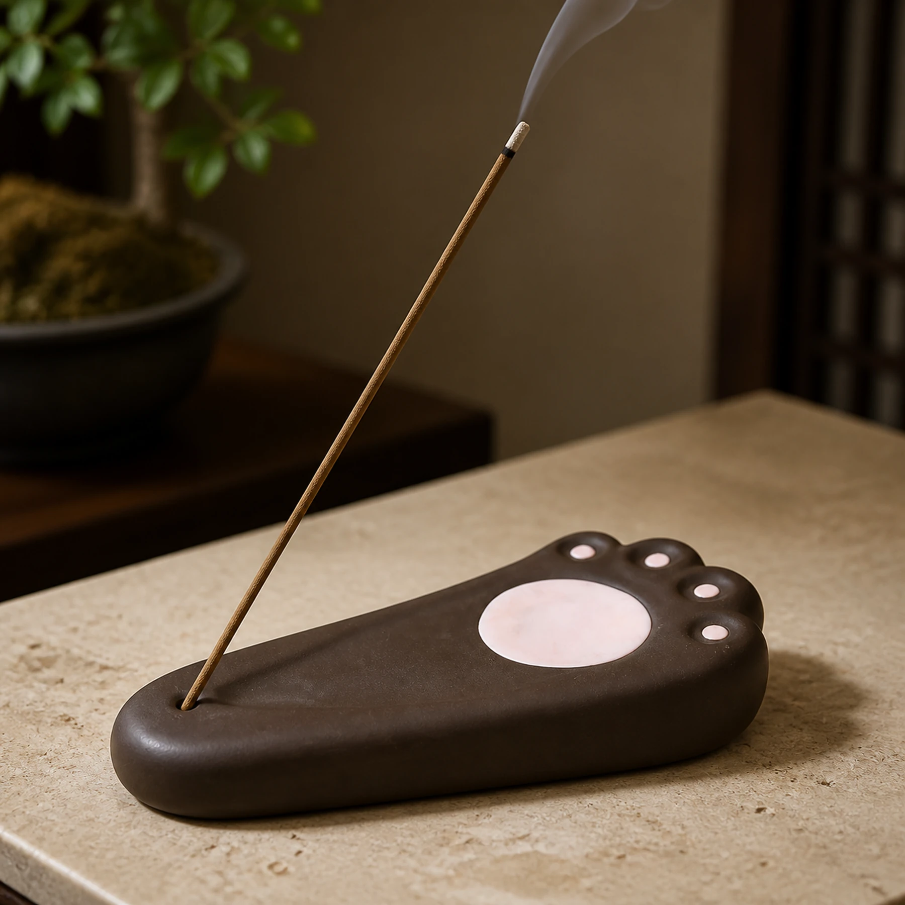 Dark brown cat paw ceramic stick incense holder with smoke rising from the stick tip