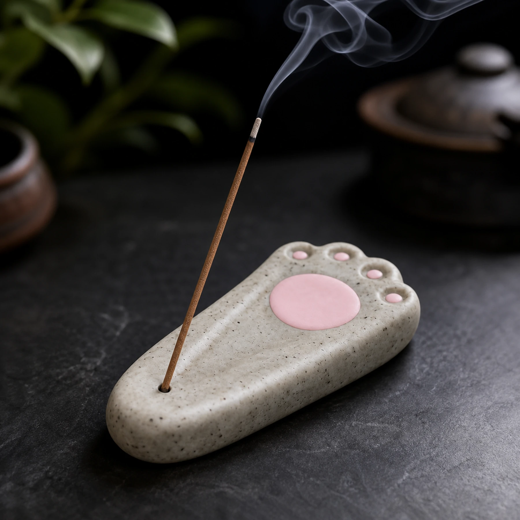 Speckled gray cat paw ceramic stick incense holder with smoke rising from the stick tip