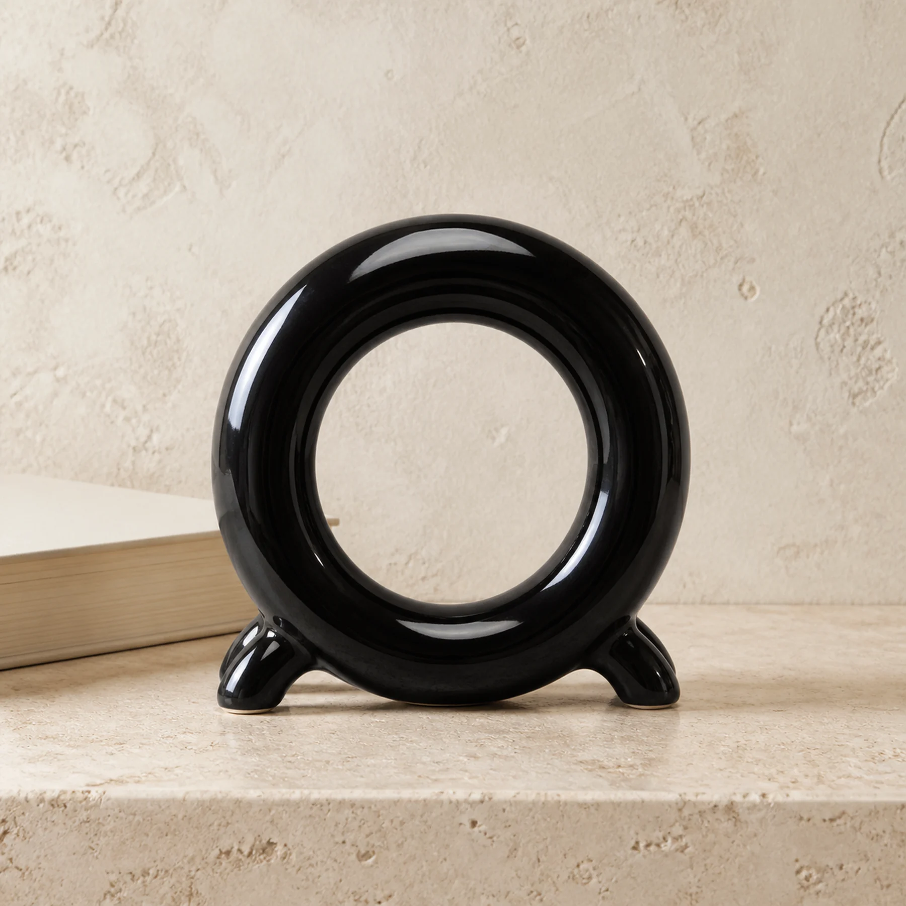 Glossy black ceramic ring storage holder on pale travertine