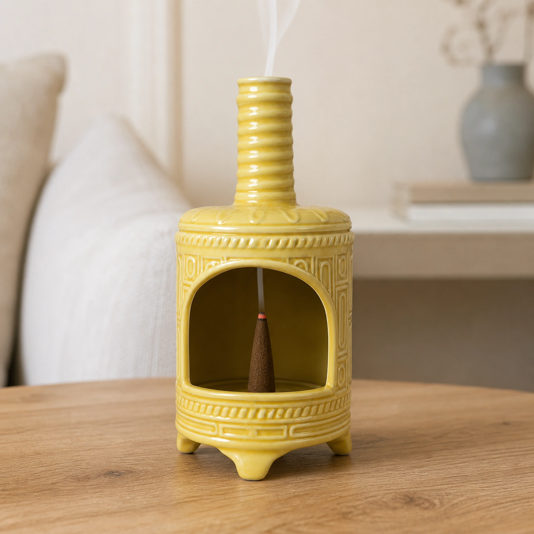 Yellow ceramic incense burner with a tapered cone ember and smoke rising through the chimney