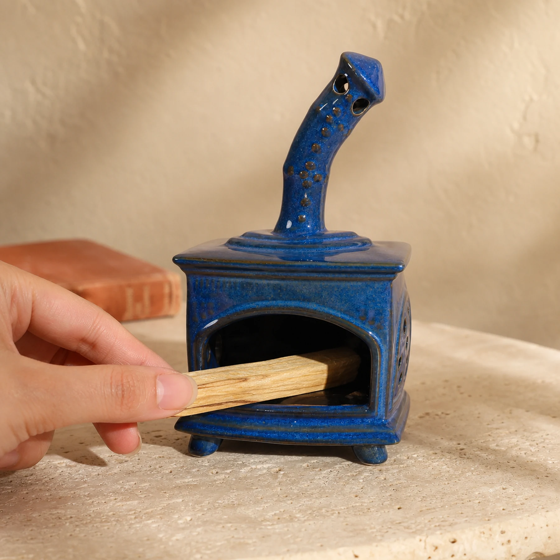 Blue ceramic fireplace incense holder with a hand placing unlit Palo Santo for scale