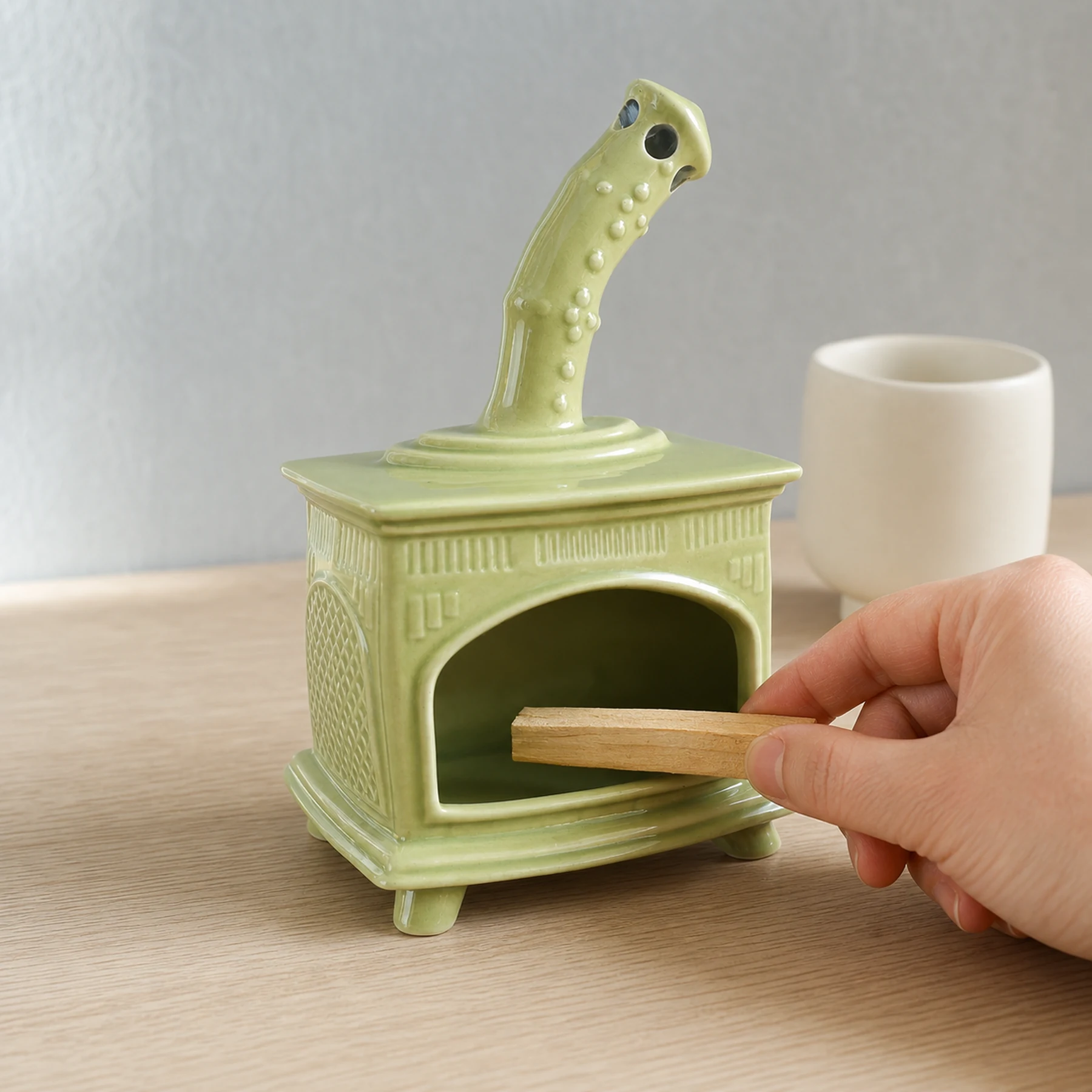 Light Green ceramic fireplace incense holder with a hand placing unlit Palo Santo for scale