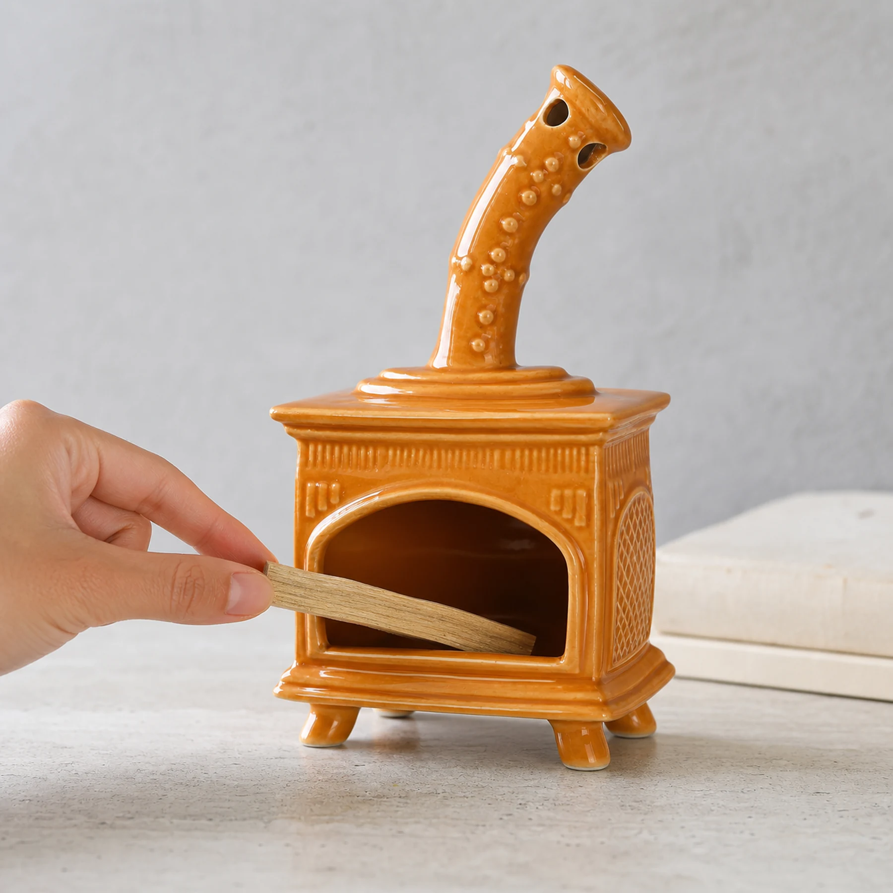 Orange ceramic fireplace incense holder with a hand placing unlit Palo Santo for scale
