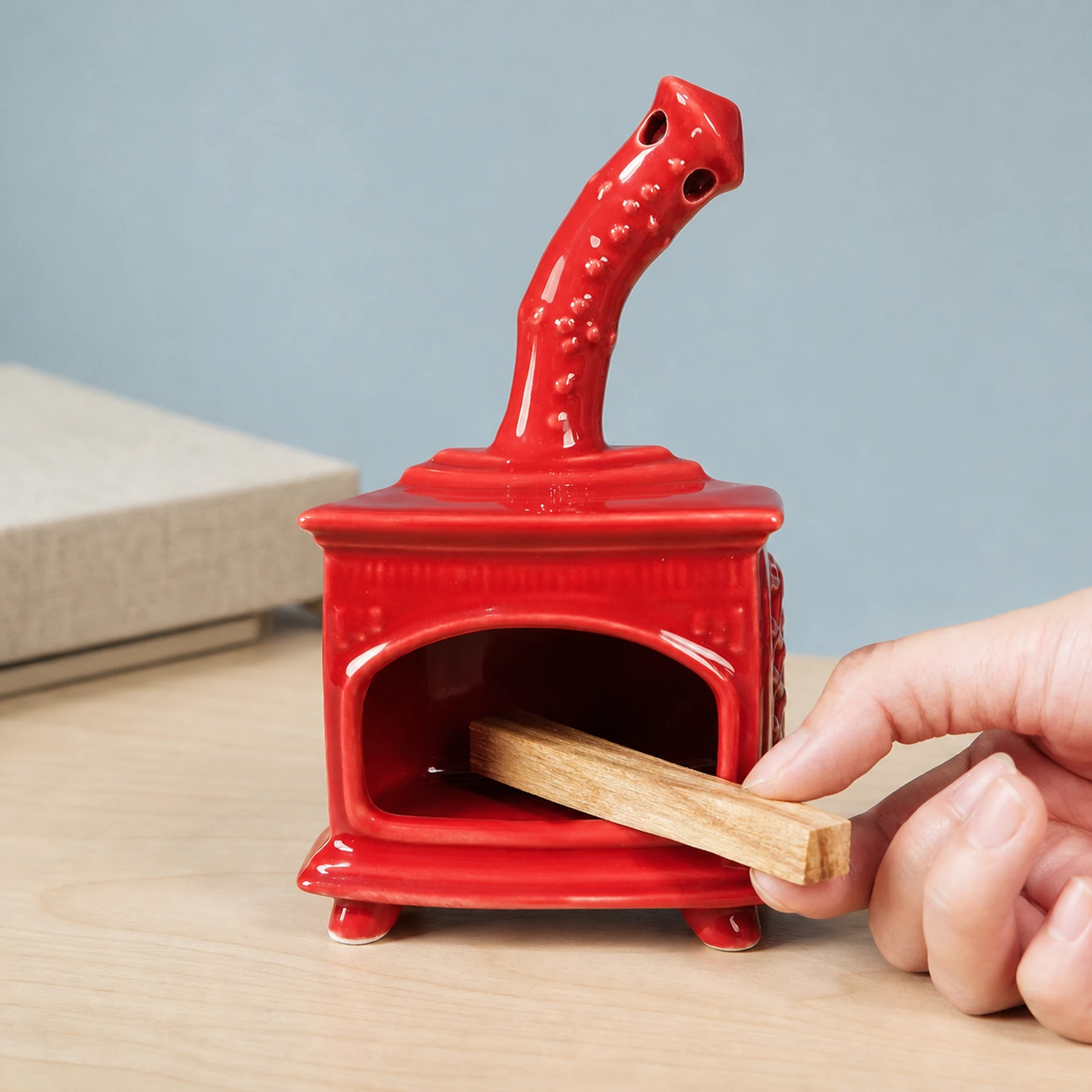 Red ceramic fireplace incense holder with a hand placing unlit Palo Santo for scale