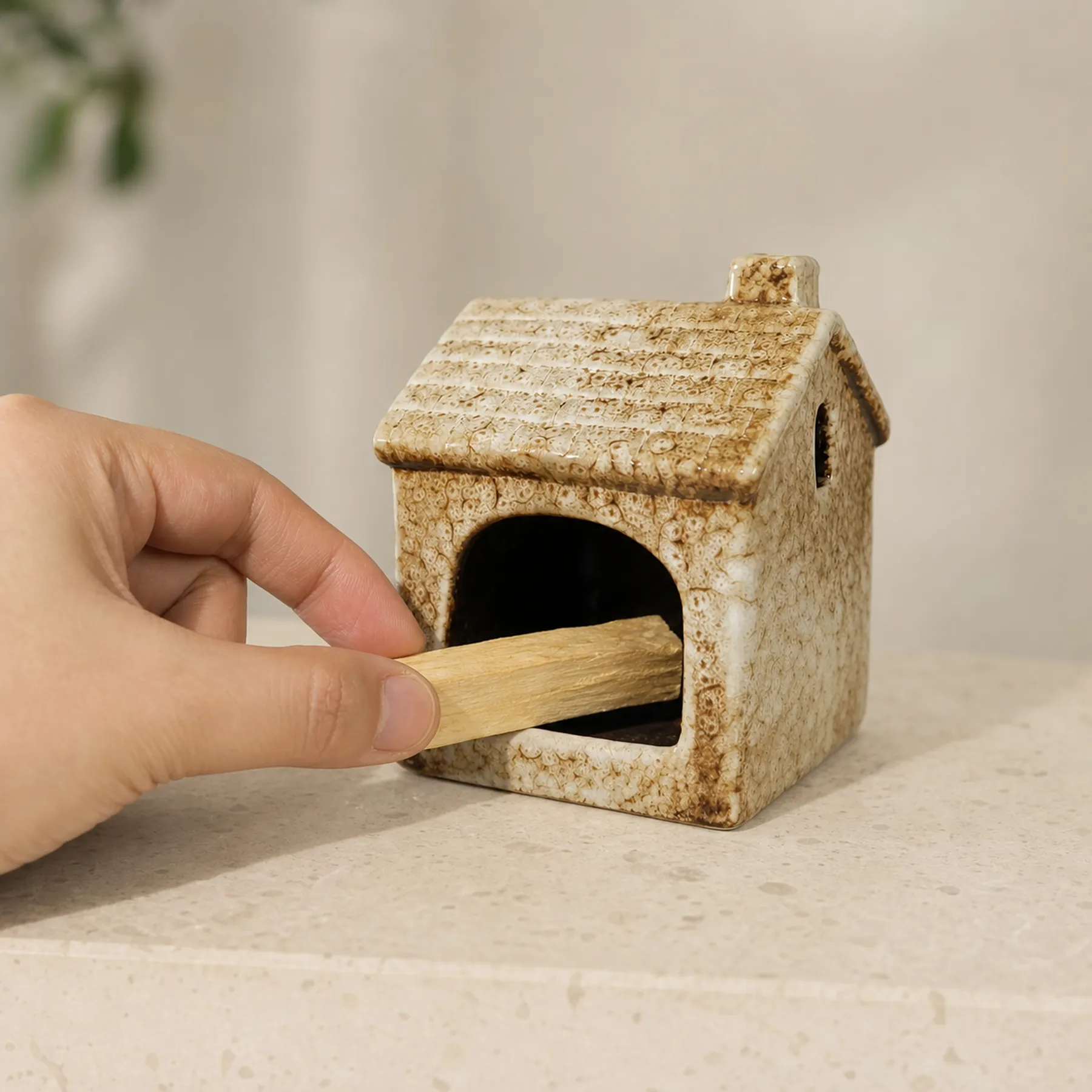 Hand placing unlit Palo Santo into Brown ceramic house holder for scale