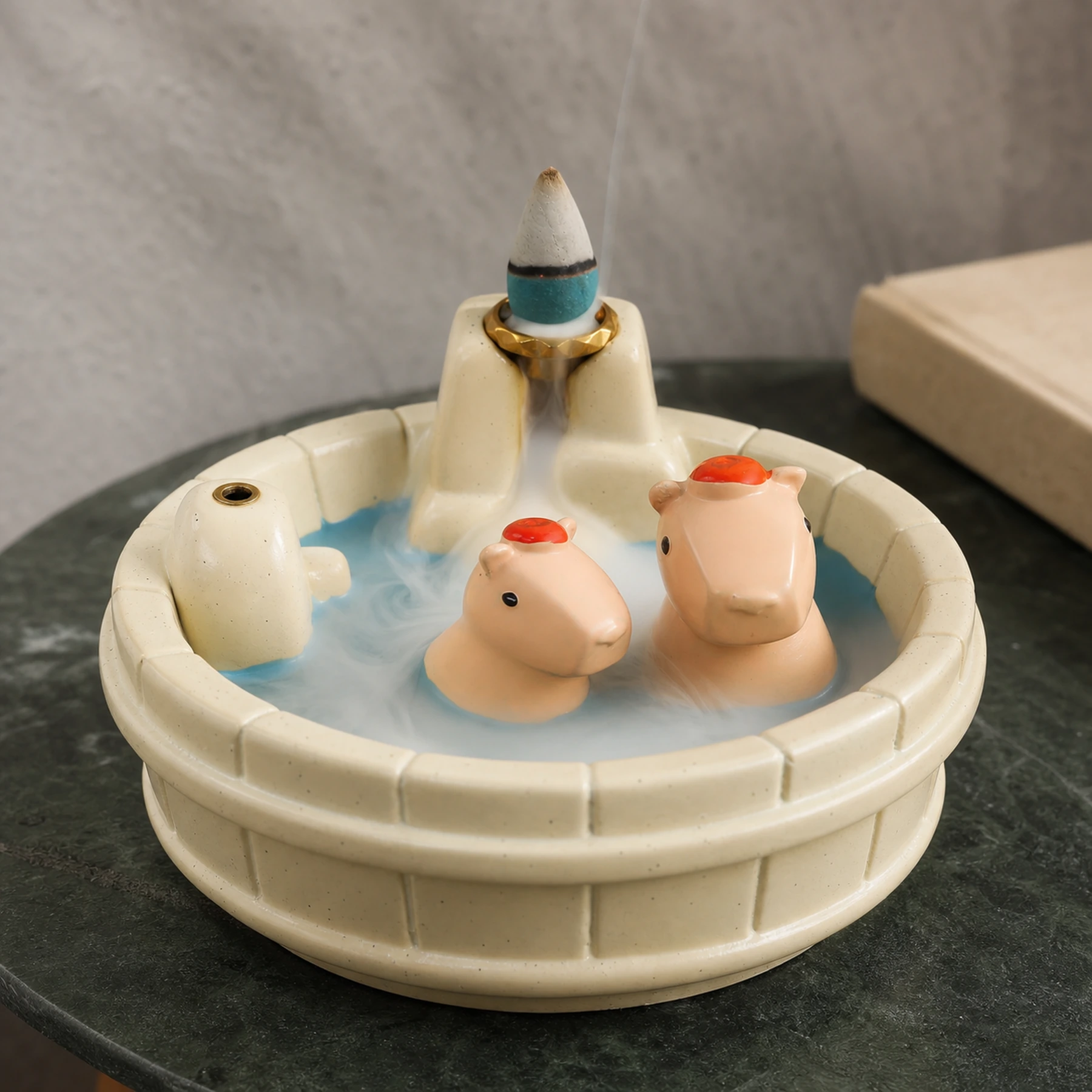 White resin capybara backflow incense burner with a smoldering cone and smoke descending through the waterfall path