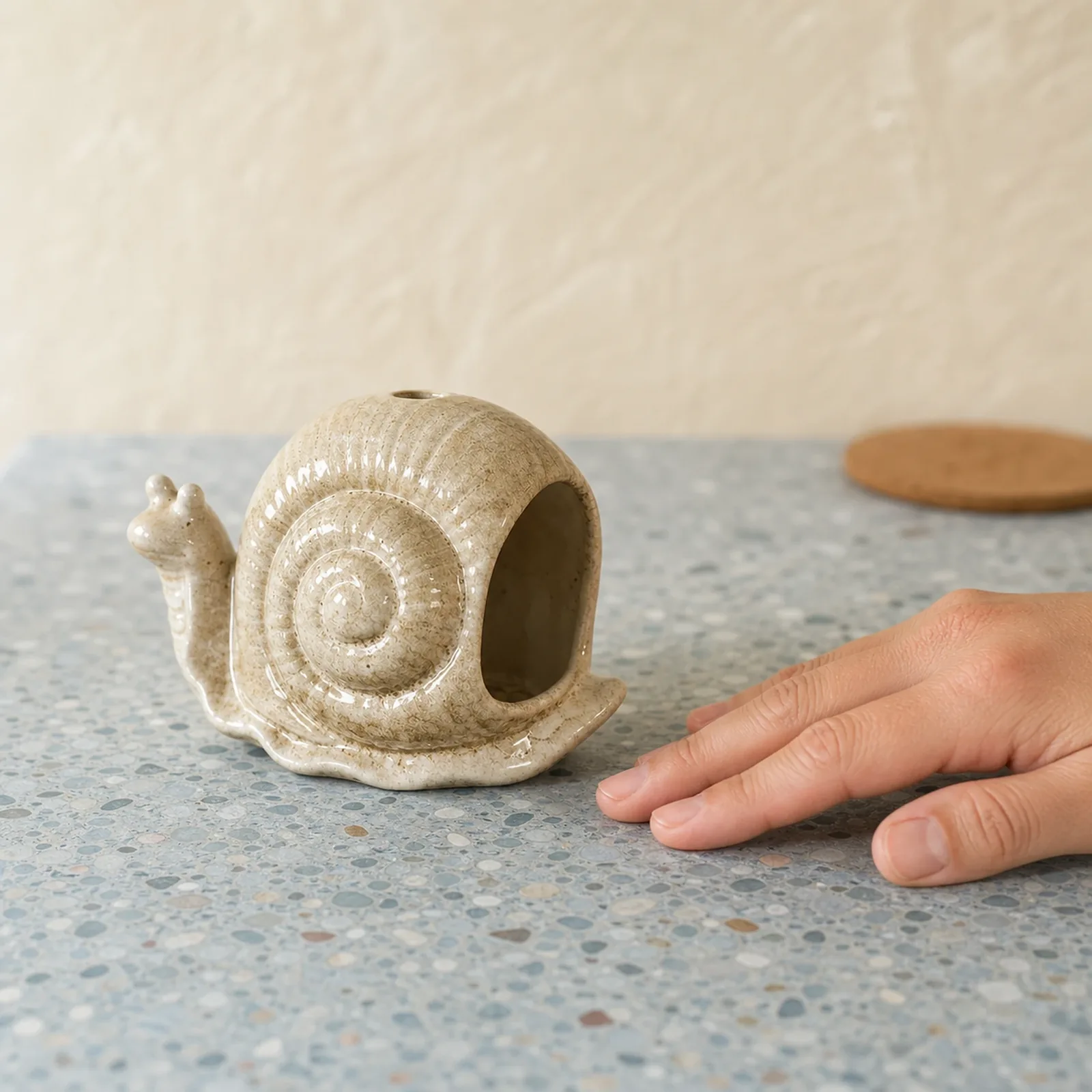 Brown ceramic snail incense holder shown at realistic tabletop hand scale
