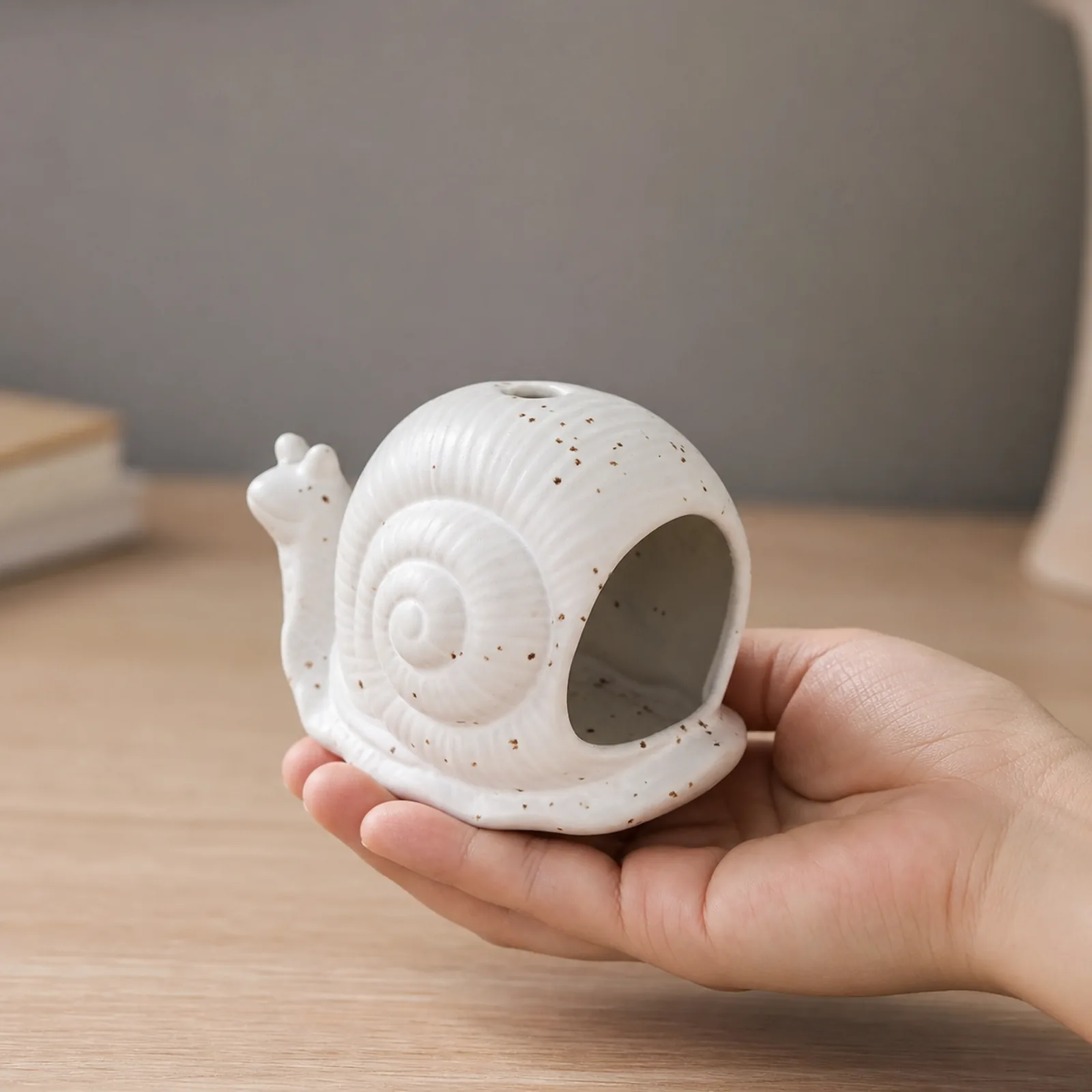 White ceramic snail incense holder shown at realistic tabletop hand scale