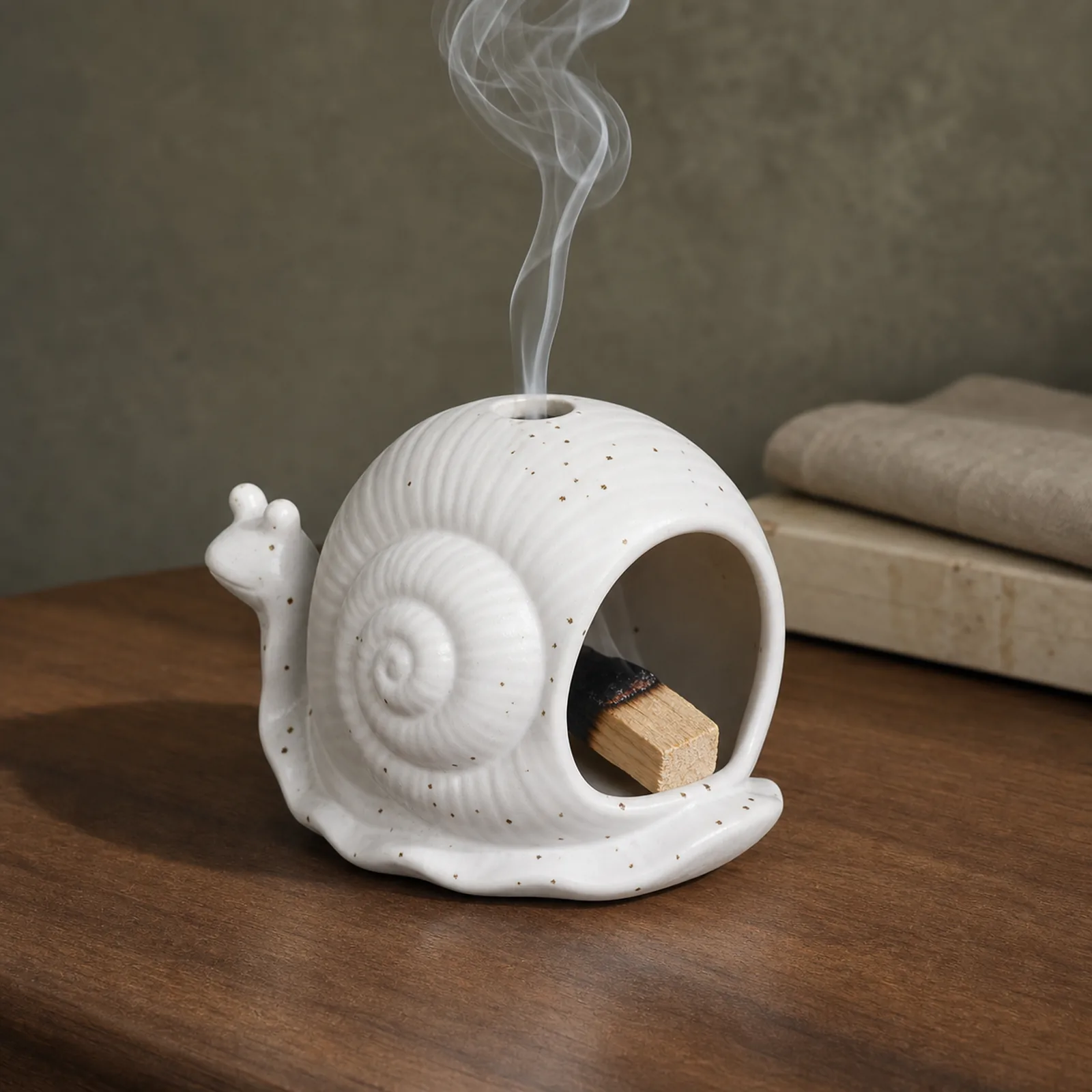 White ceramic snail Palo Santo holder with a visible charred ember and thin smoke rising through the top vent