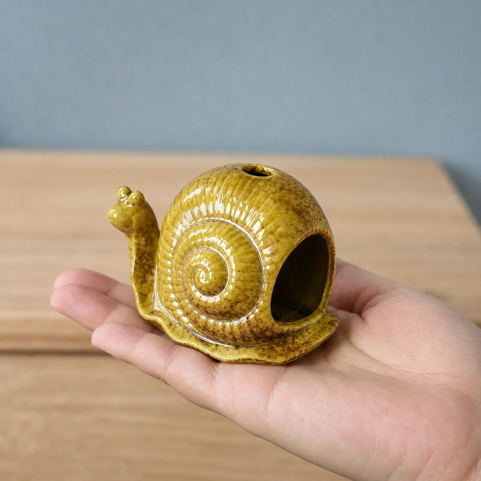 Yellow ceramic snail incense holder shown at realistic tabletop hand scale