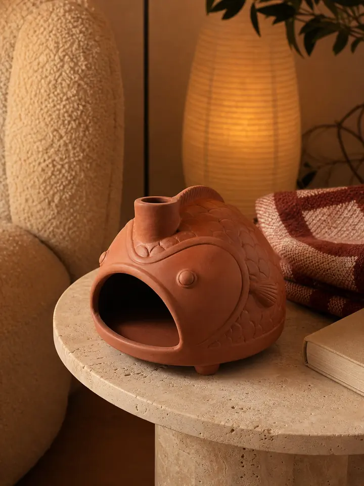 Terracotta fish incense burner styled in a warm evening reading corner