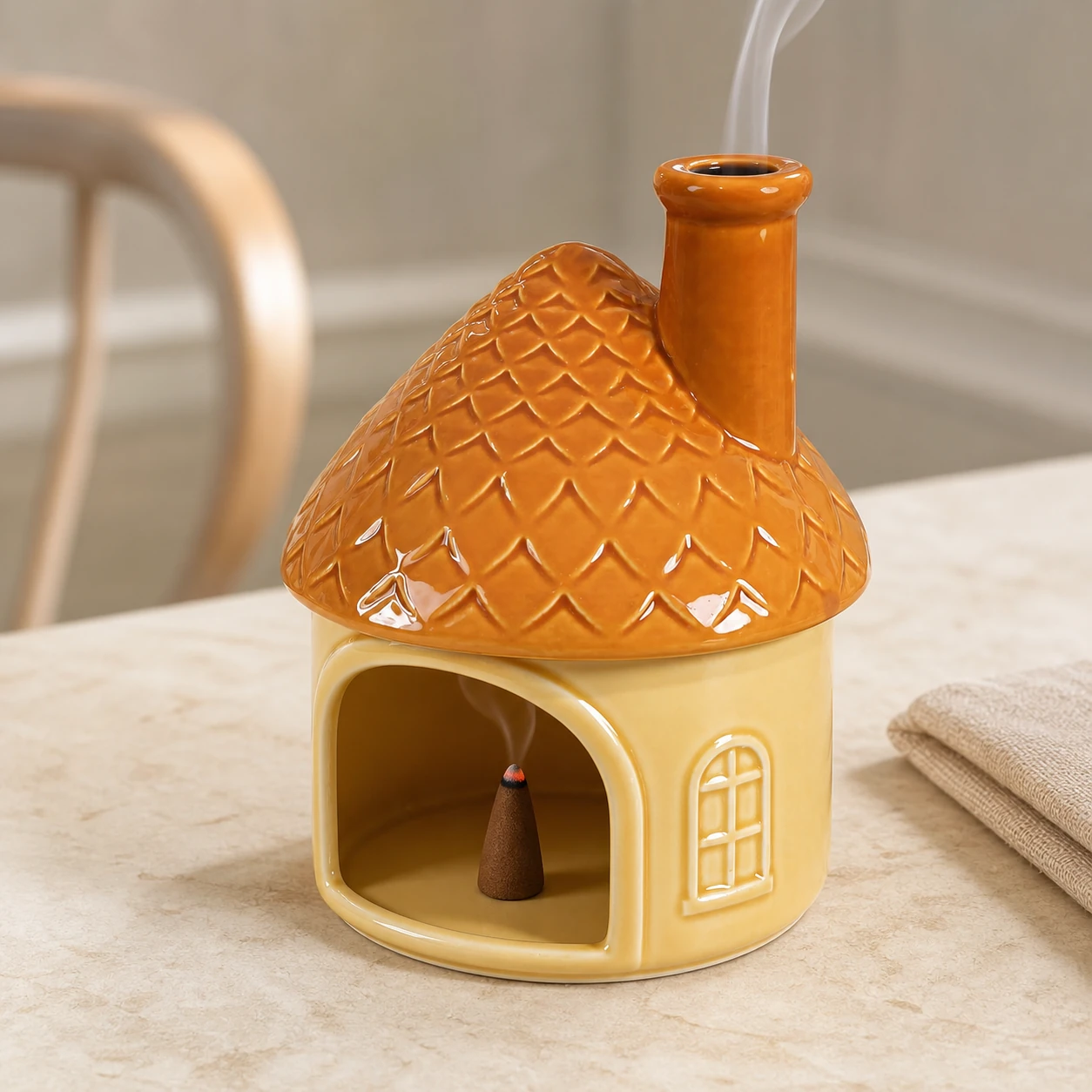 Yellow house ceramic Palo Santo holder with a smoldering tapered incense cone inside and smoke exiting the chimney