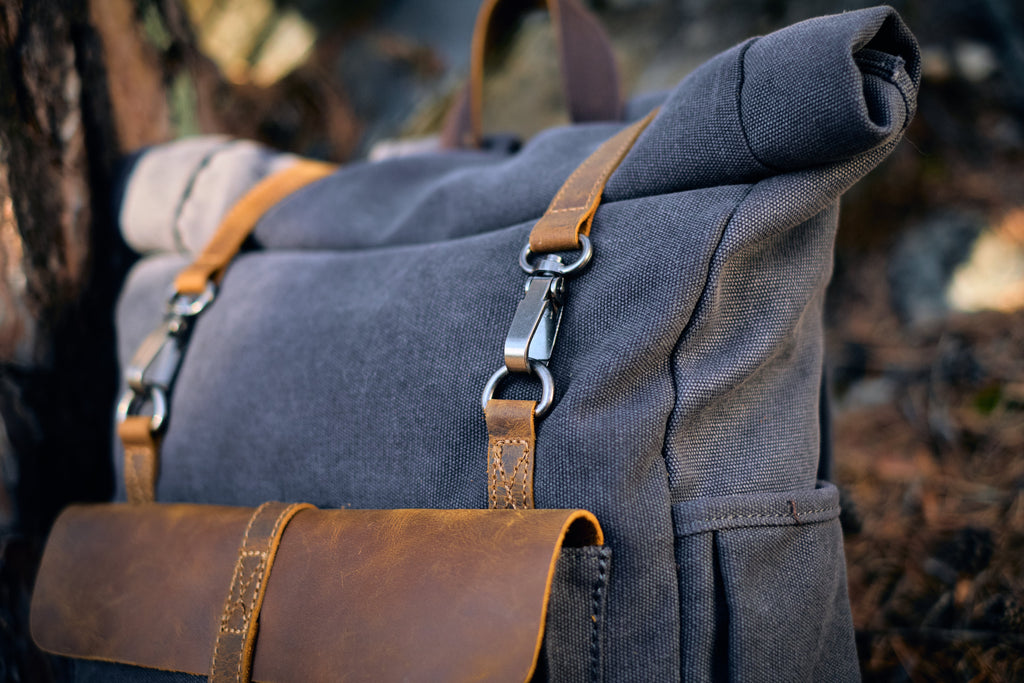 vintage canvas and leather book-bag with padding hanging against a tree