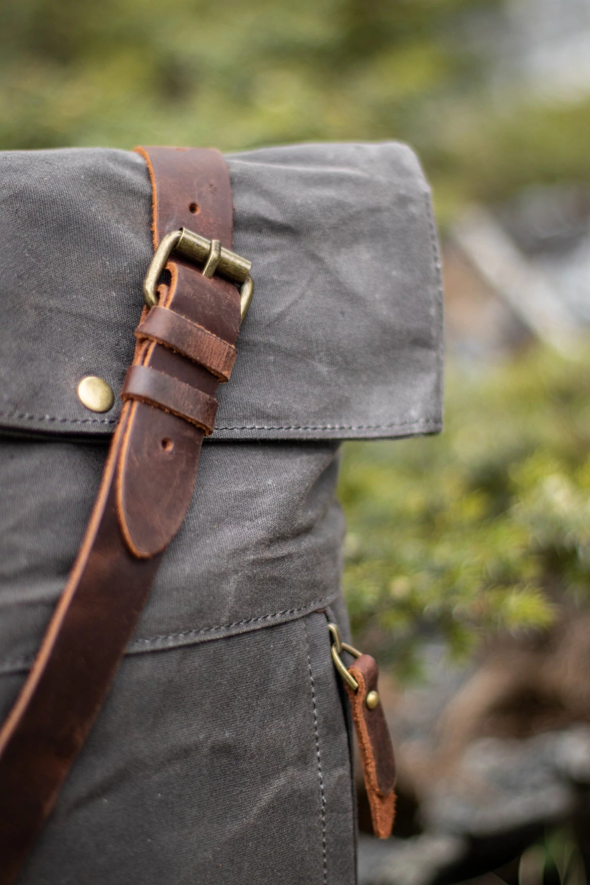 Macro of the top flap full-grain leather strap with brass roller buckle and shoulder strap routing on the Oslo dark grey rucksack