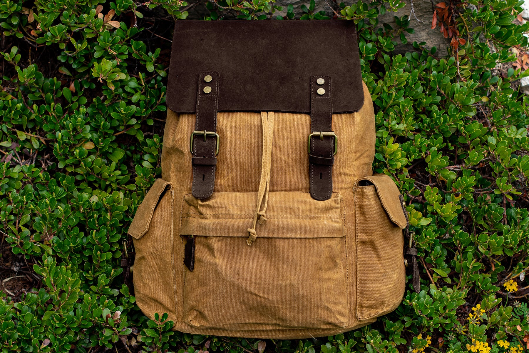 quality leather and waxed canvas backpack in khaki colors sitting on a field of wild grass outdoor