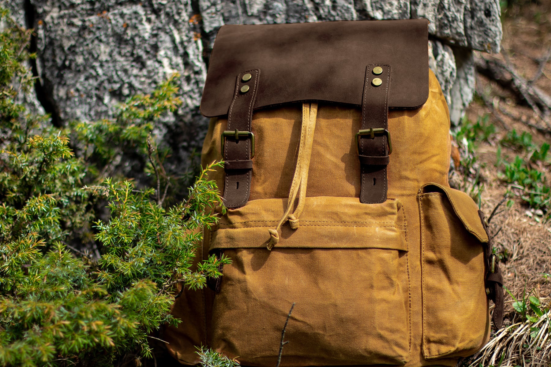 best vintage-style travel waxed canvas and leather backpack for men and women with a padded laptop sleeve laying on a rock