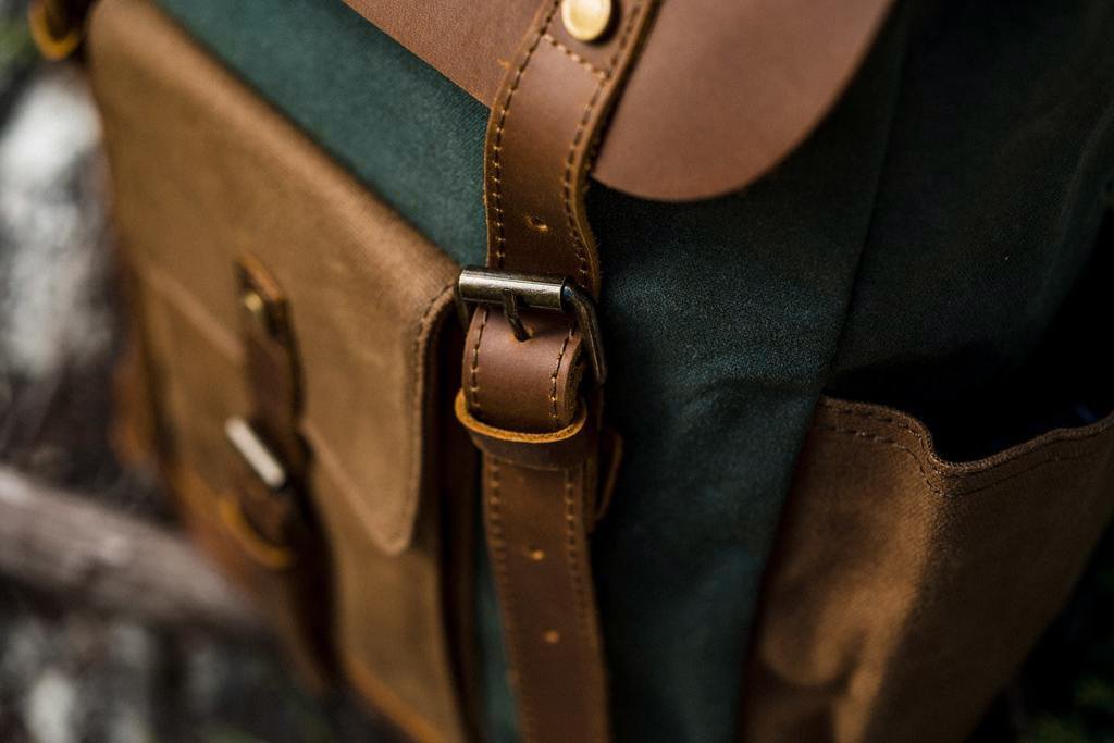 Vue rapproch&eacute;e sur les sangles en cuir. le rabat en cuir et les boucles magn&eacute;tiques d'un sac &agrave; dos baroudeur vintage en toile cir&eacute;e et cuir authentique