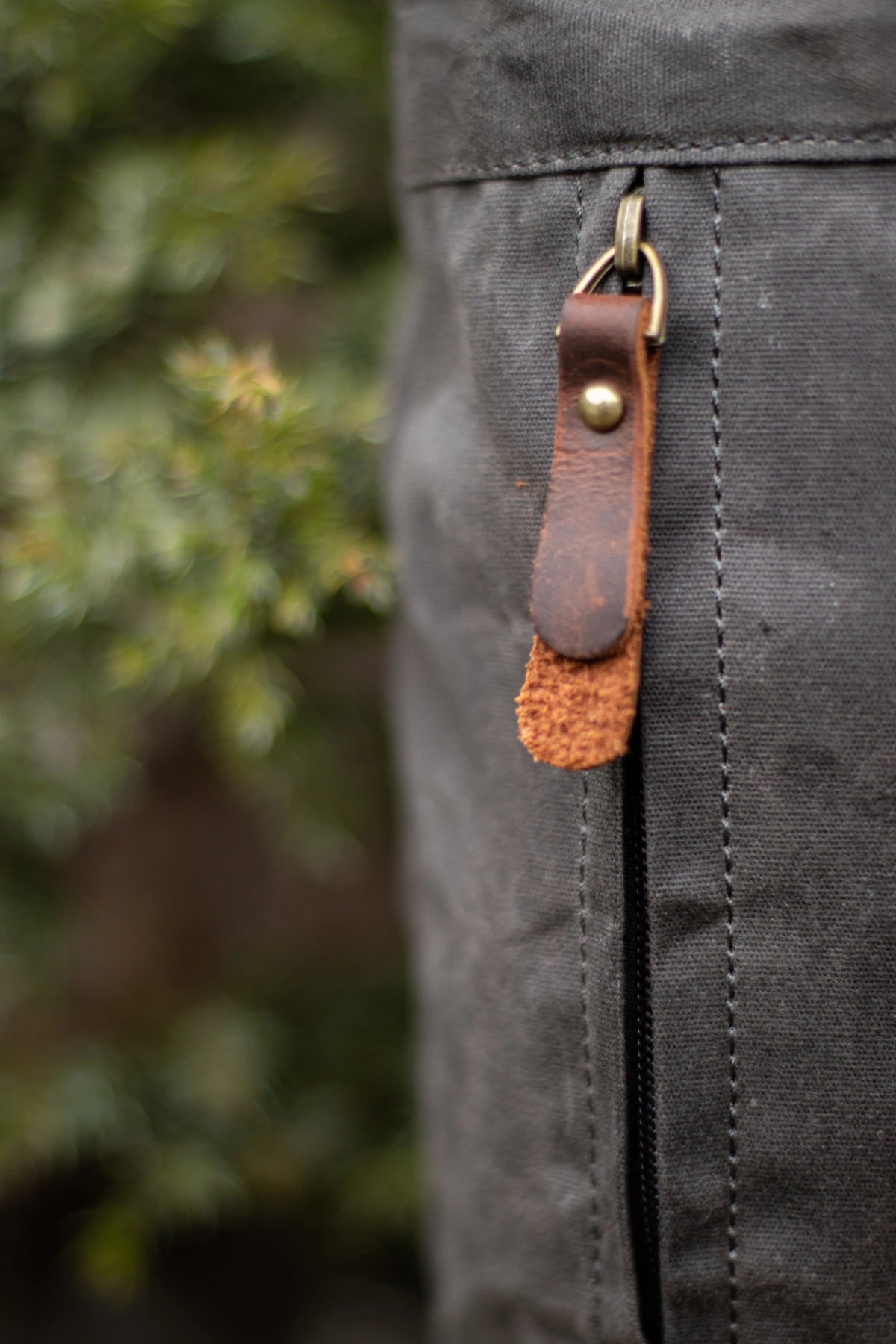 Close-up of the side YKK zipper pull with full-grain leather tab and antiqued brass D-ring on the Oslo dark grey waxed canvas rucksack