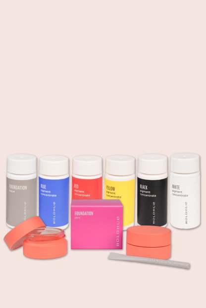 a grouping of six cartridges in base, blue, red, yellow, black and white, and an accessory kit of foundation pink storage jars and a small spatula to mix