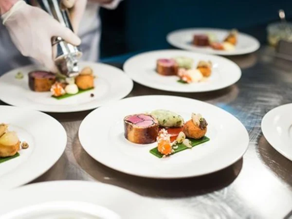 vb_hospitality A chef presents gourmet dishes on a restaurant plate and artfully arranges meat and side dishes in a professional kitchen.