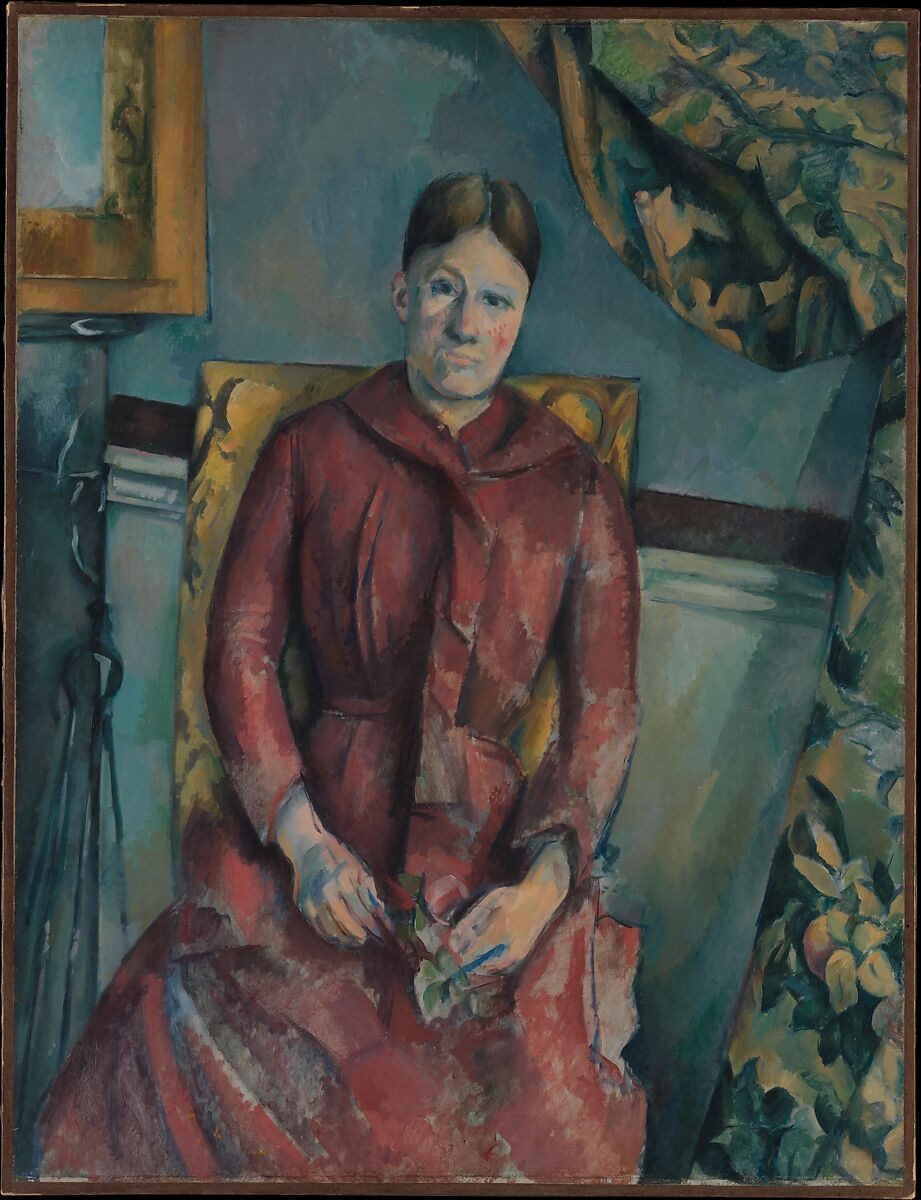 A seated woman wears a red dress in a yellow chair against a mottled blue-green wall, with patterned curtains and darker furniture around her.