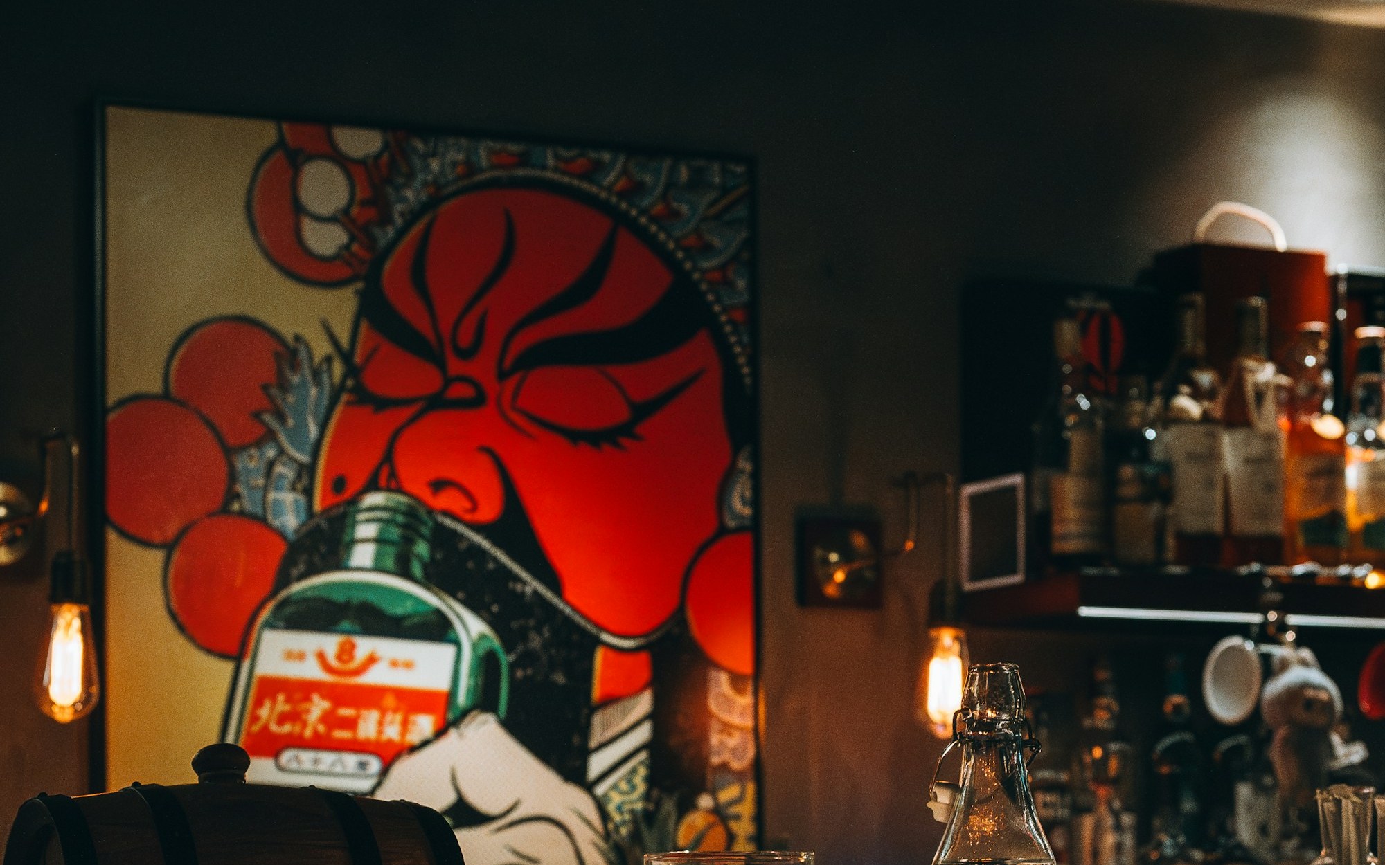Real dimly lit bar counter with a large red artwork behind the bottles and glasses.