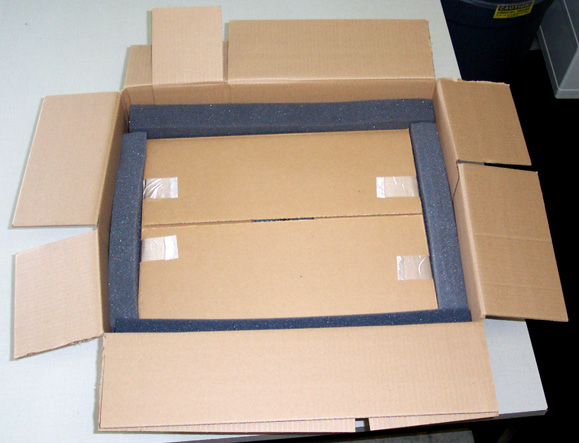 A closed inner cardboard box rests inside a larger open box with dark foam separating the boxes.