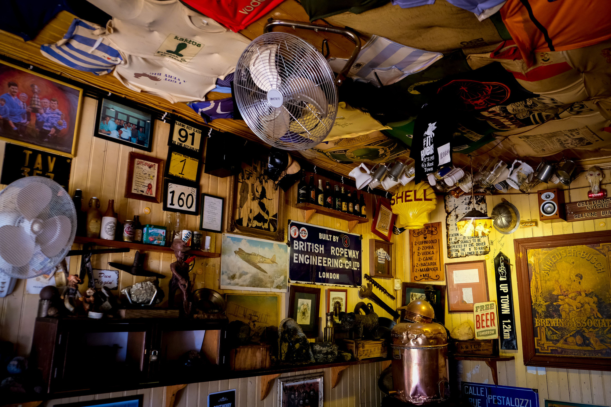 A pub interior with framed pictures, old signs and memorabilia on wood-paneled walls, with shirts hanging across the ceiling.
