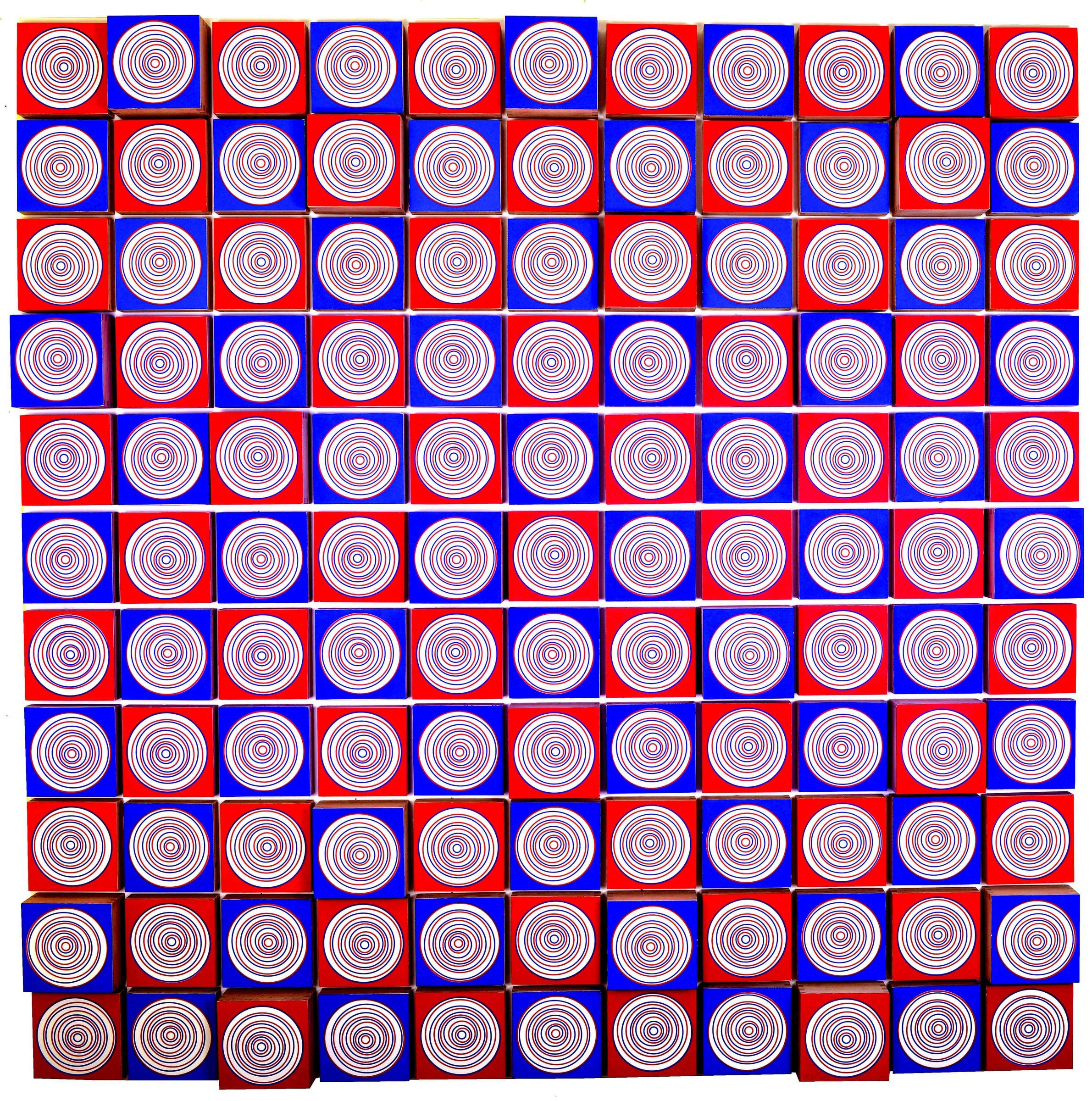 A red and blue grid of wooden squares painted with concentric colored rings; lower squares project and cast shadows.