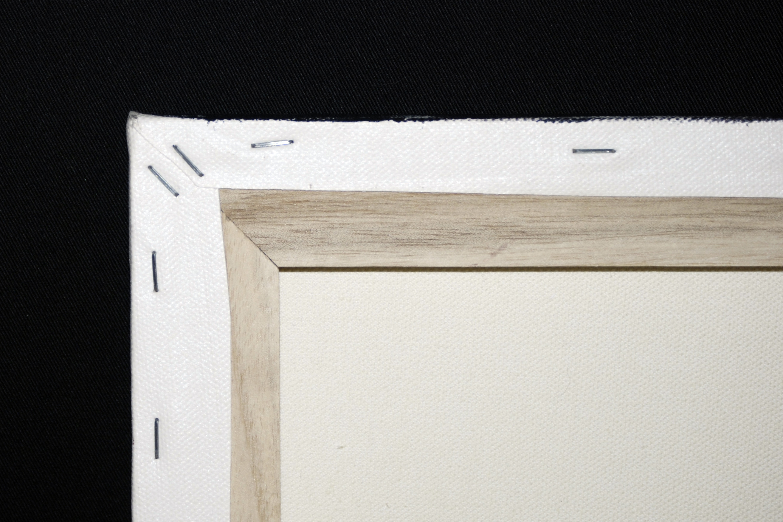 The reverse corner of canvas shows white fabric folded and stapled over two joined wooden stretcher bars.
