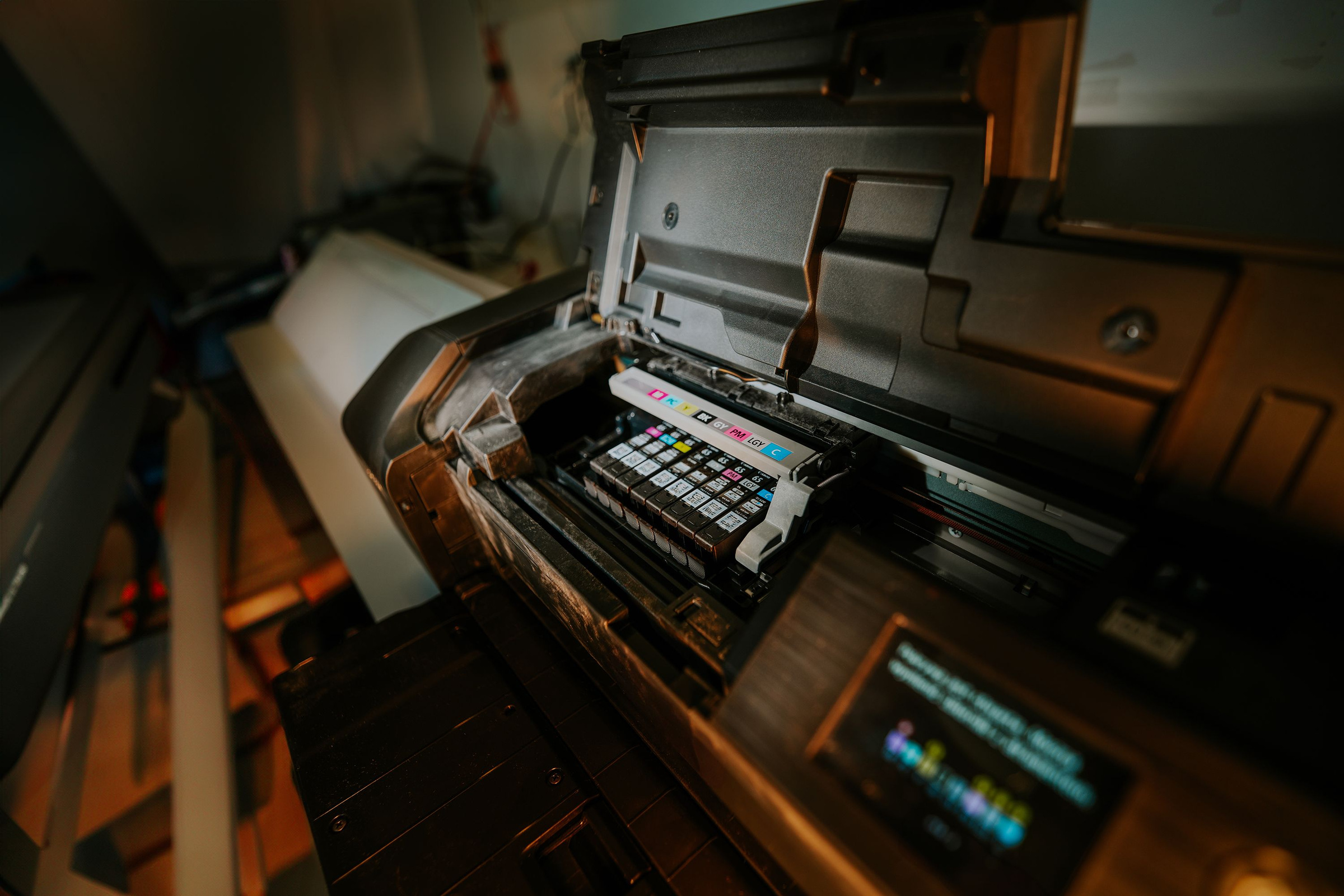An open inkjet printer reveals a row of color ink cartridges beneath its raised cover.
