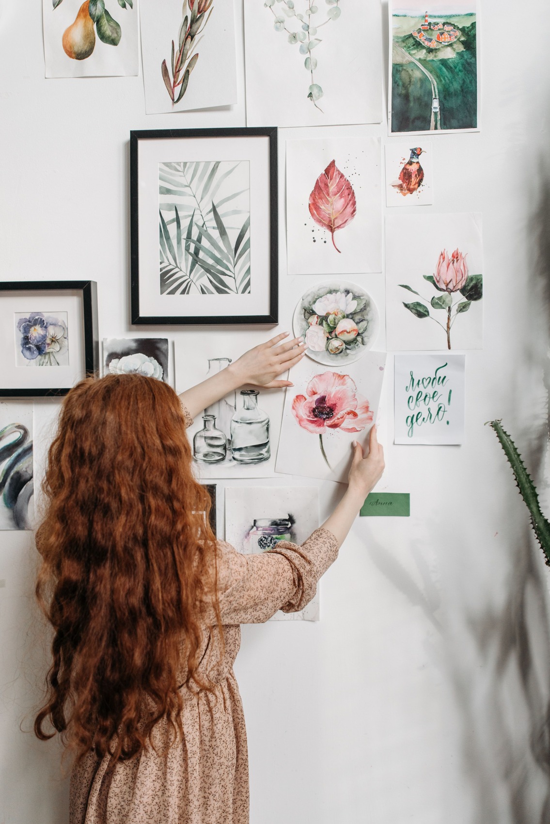 A person positioning a drawing on paper beside other wall pictures.
