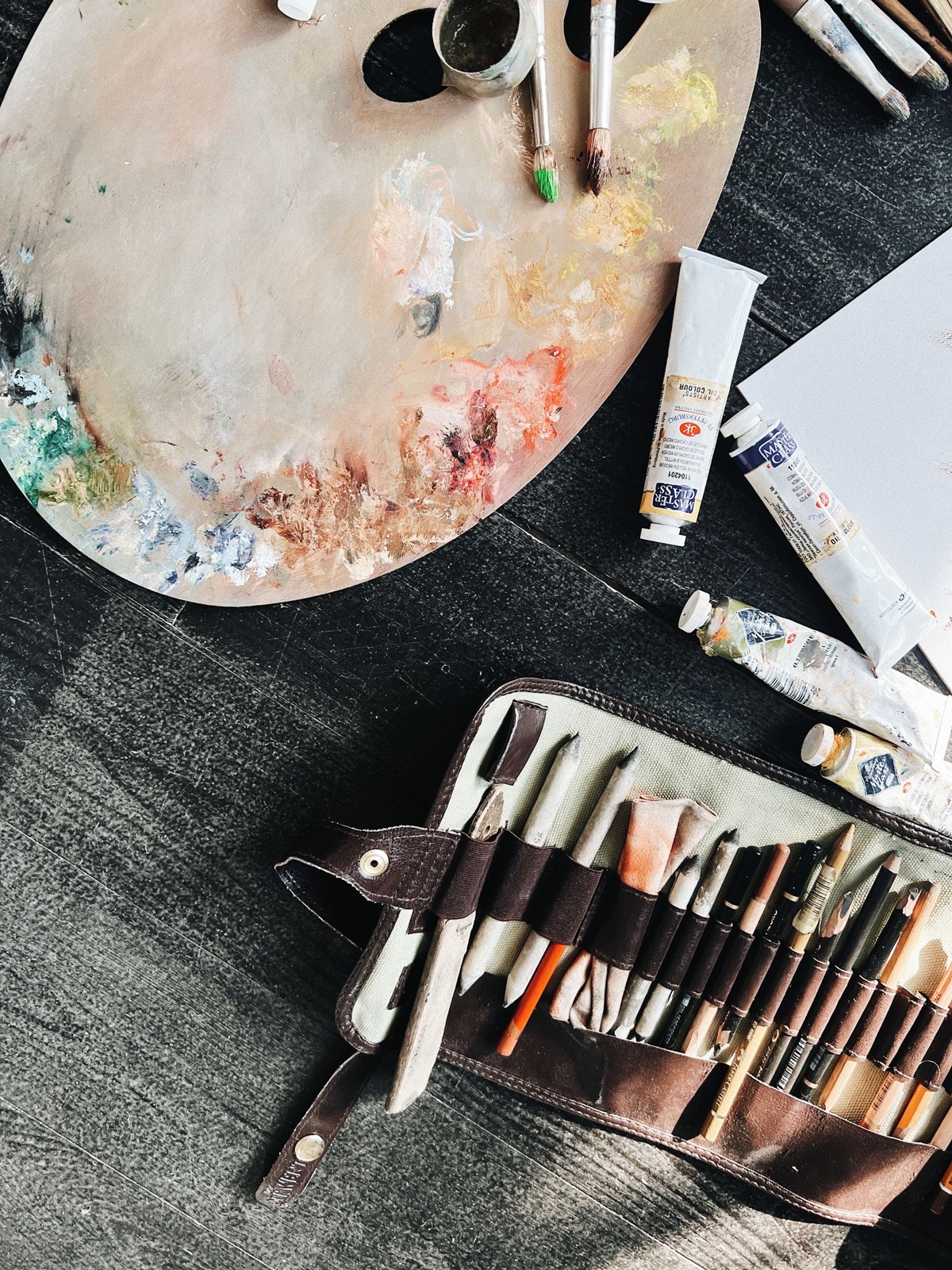 Paint tubes beside a mixing palette and a case of brushes.