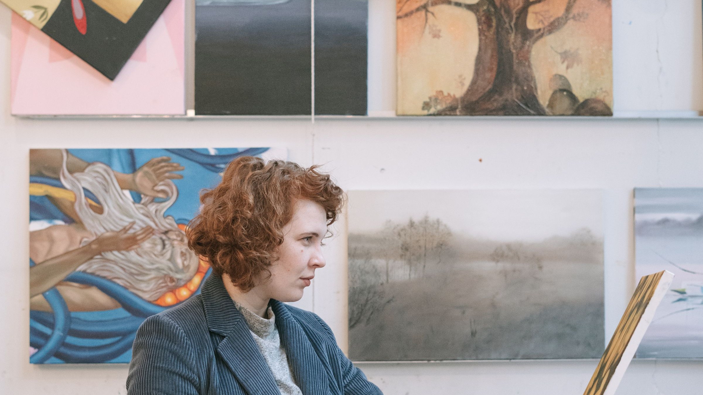 Artist in a studio examining a canvas painting among other artworks. Photo by Ivan S via Pexels.