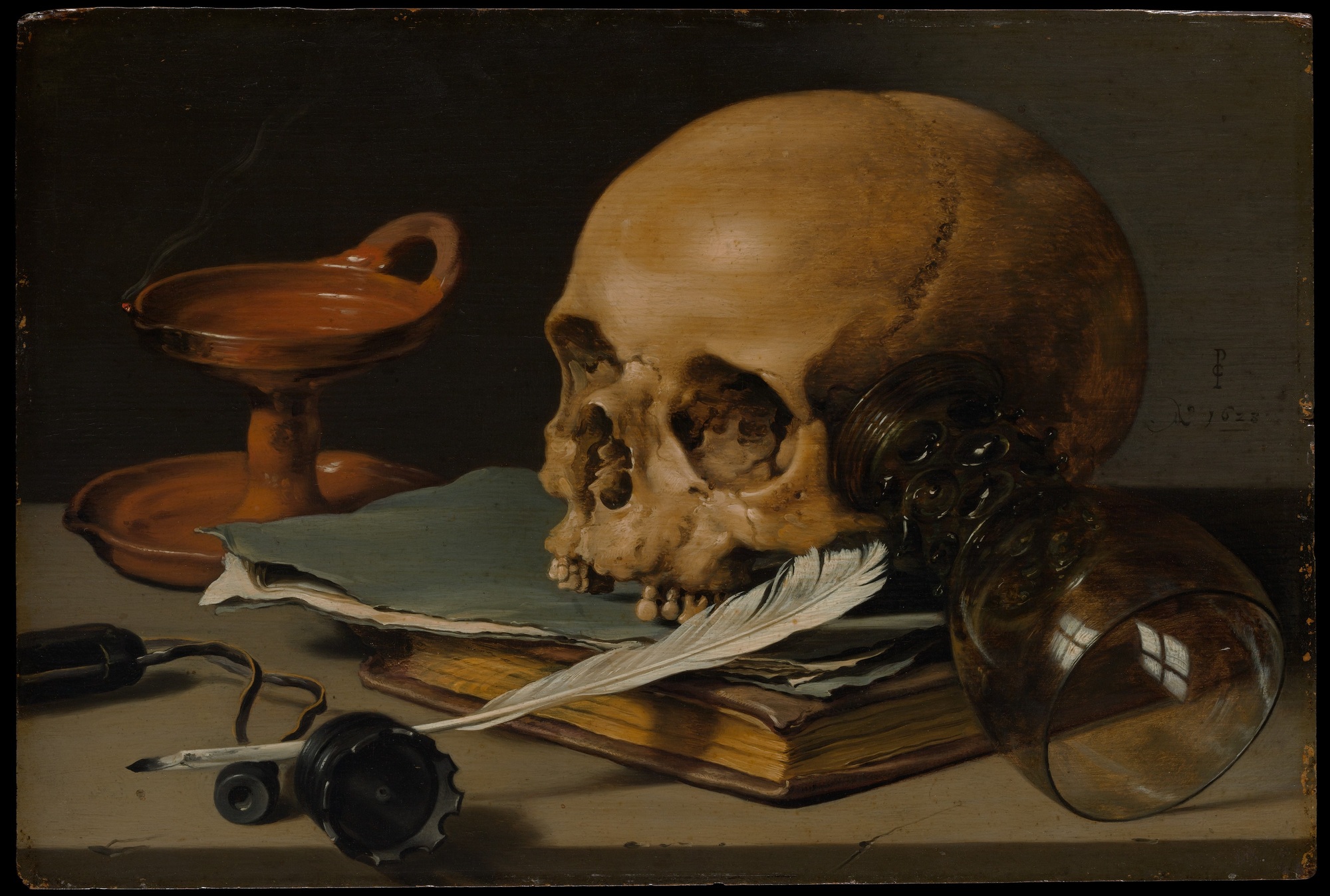 A skull rests on a book beside a white writing quill, an overturned glass and a smoking oil lamp on a tabletop.