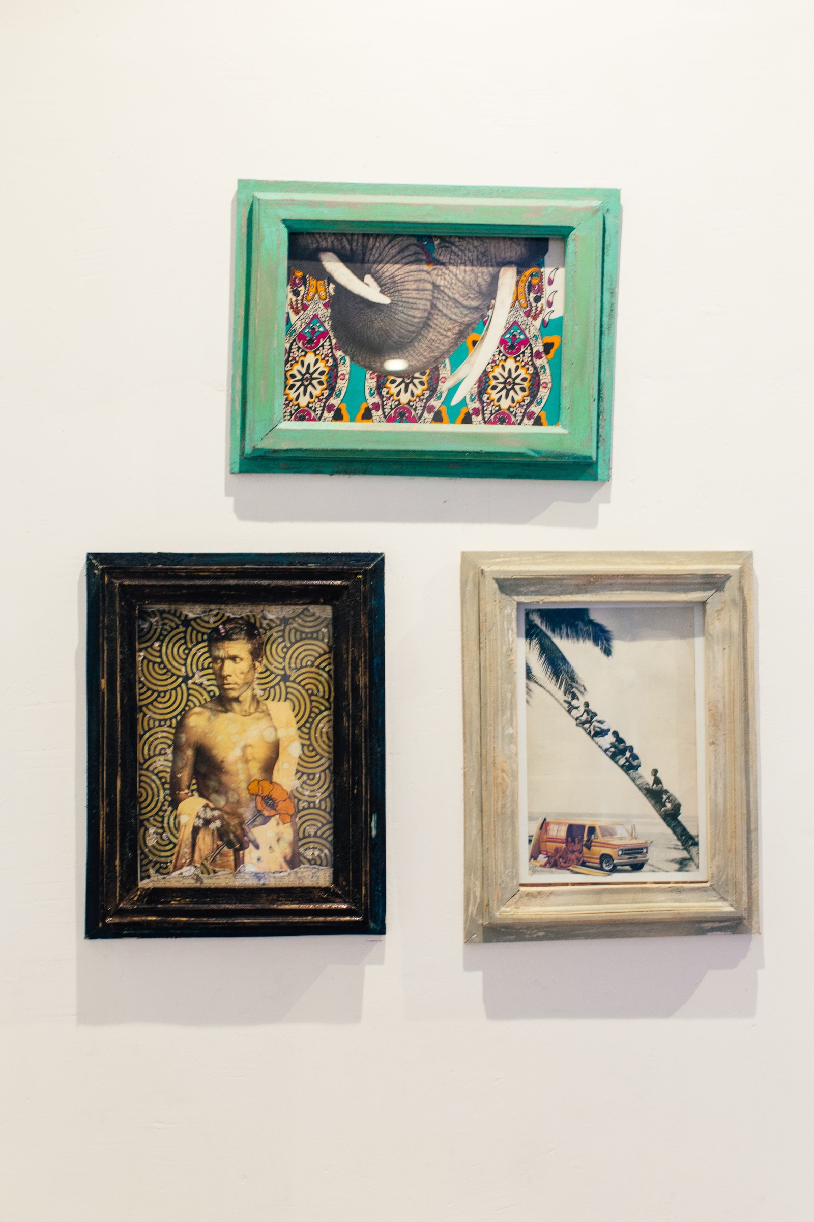 Three pictures in green, dark and pale wood frames hang on a white wall.