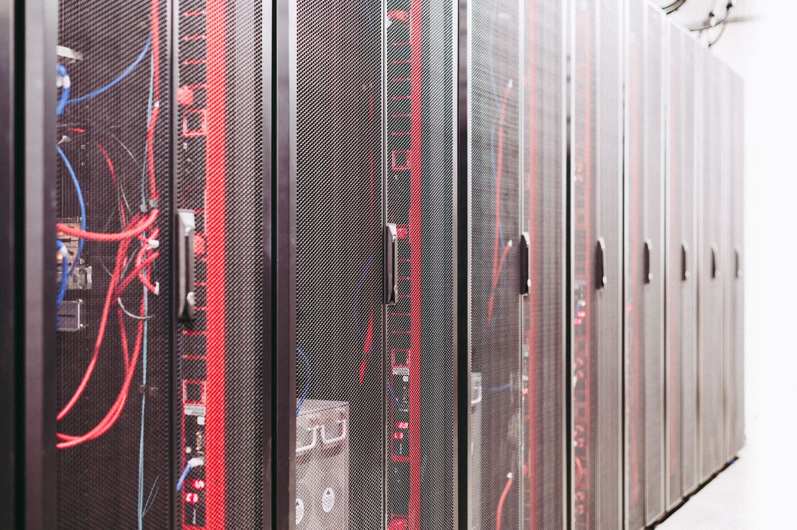 Rows of black server cabinets with red and blue network cables behind perforated doors.