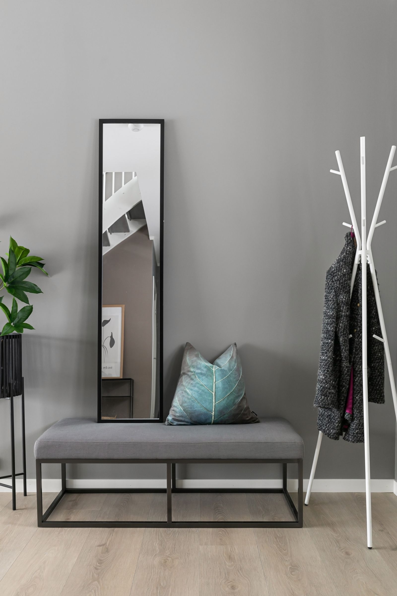 A tall mirror leaning over a bench near a freestanding coat rack, showing a function-led entry arrangement.
