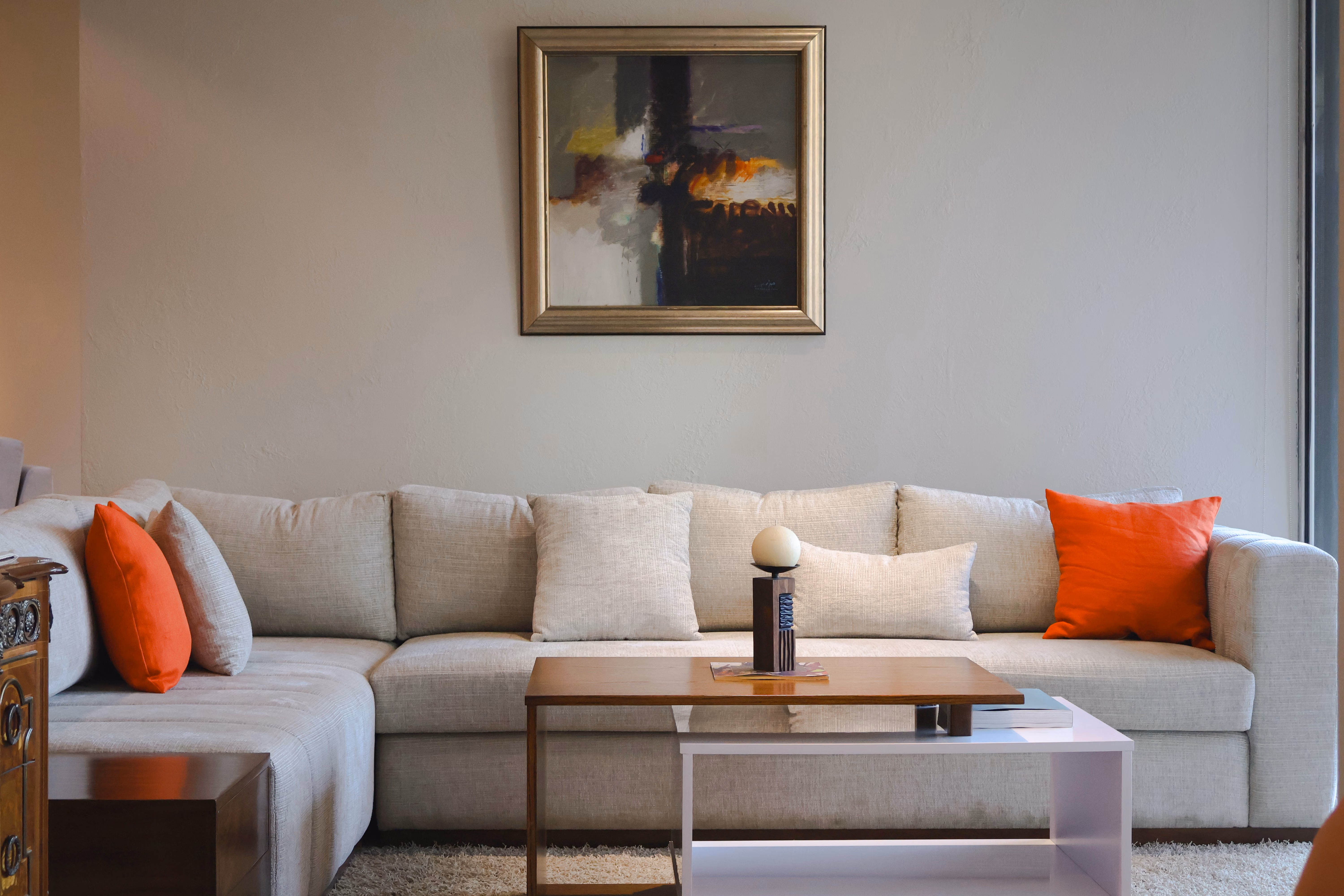 Contemporary living room with a beige sofa, orange pillows, and framed abstract artwork.