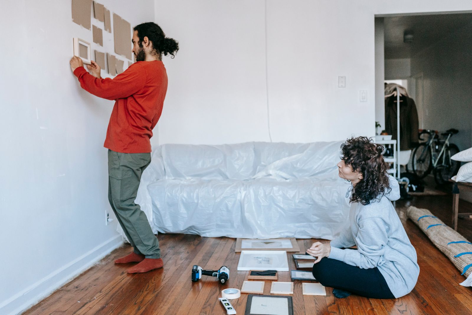 Two people using paper templates and frames to plan a picture arrangement on a wall before hanging.