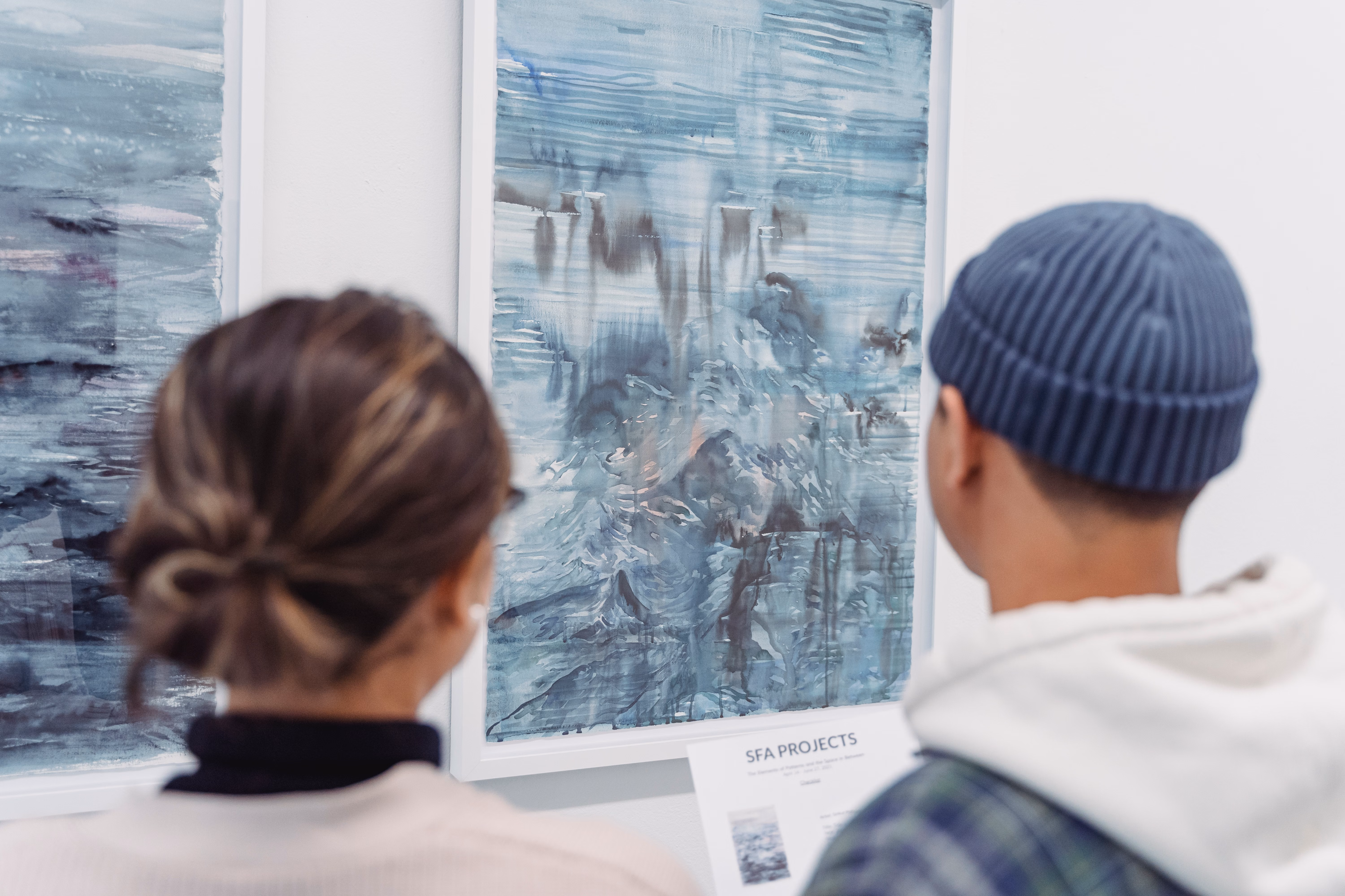 Two visitors standing beside framed abstract paintings in a quiet gallery.