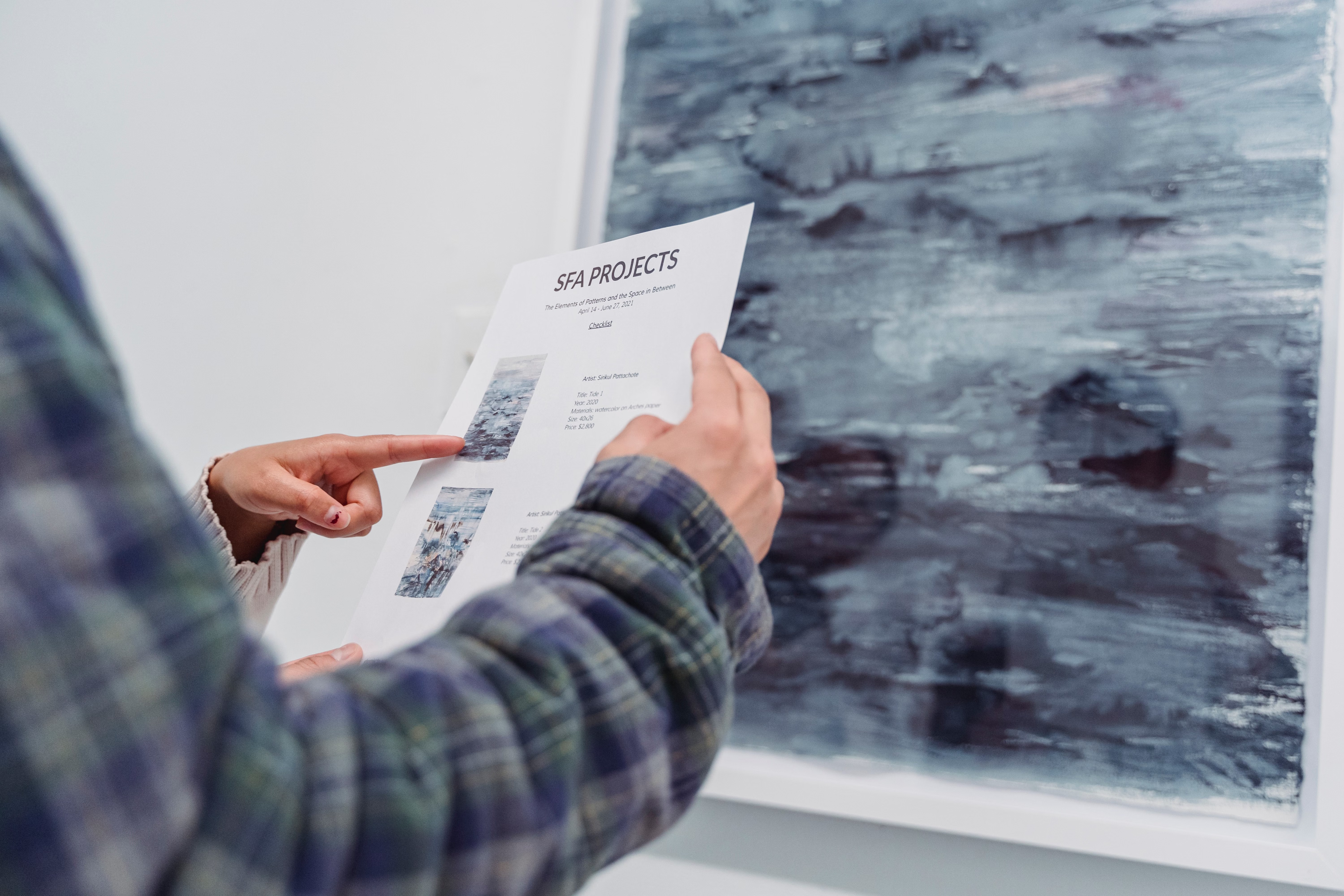 A person holding a gallery document while looking at a large abstract artwork, illustrating careful visual observation.
