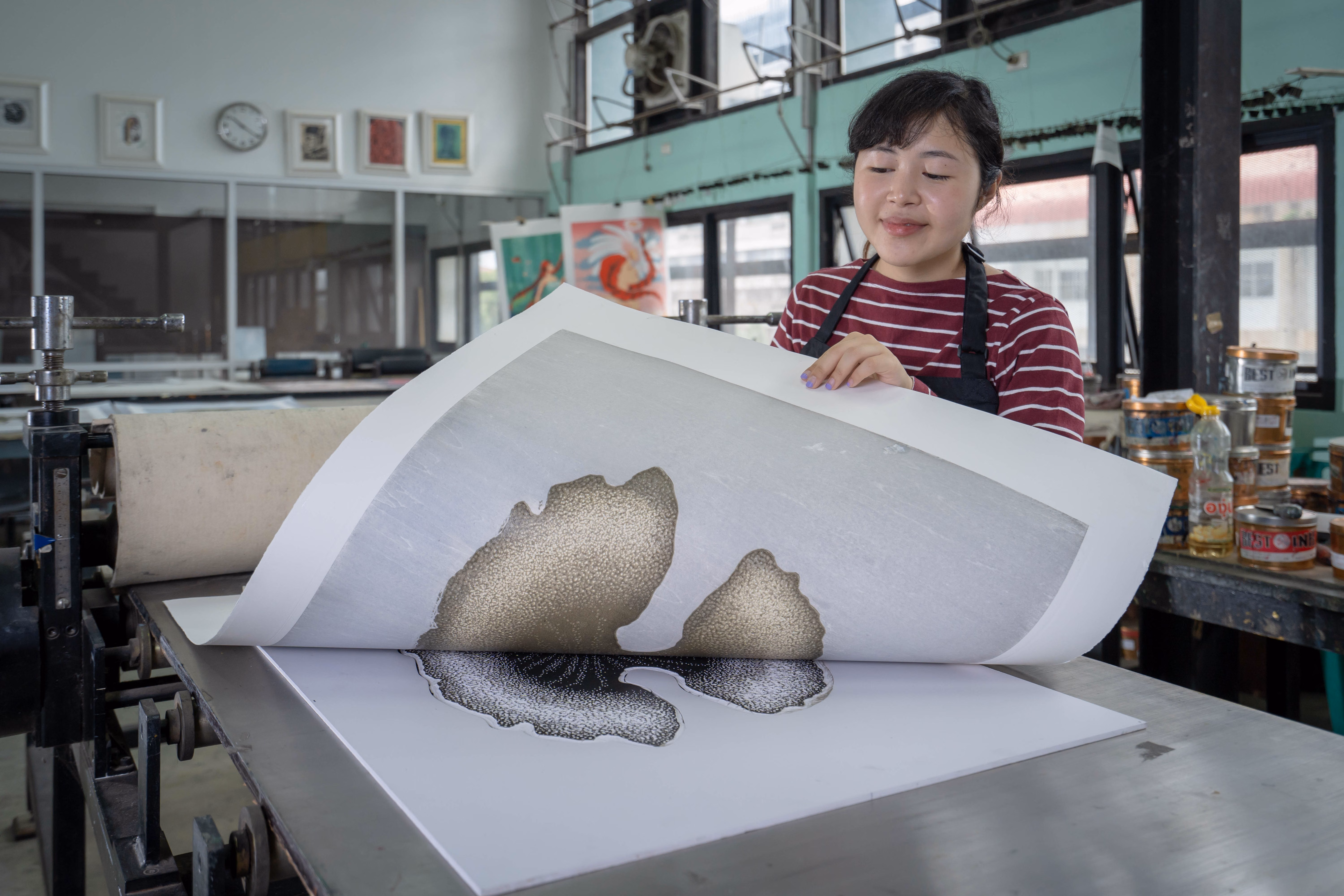 An artist lifts a fresh print from a large press in a printmaking studio.