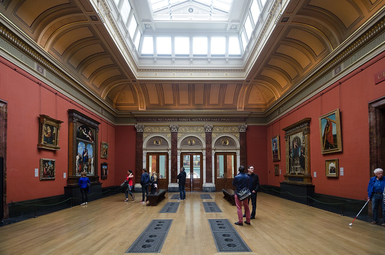 Framed paintings on red walls beneath the skylight in the National Gallery’s Central Hall, London.