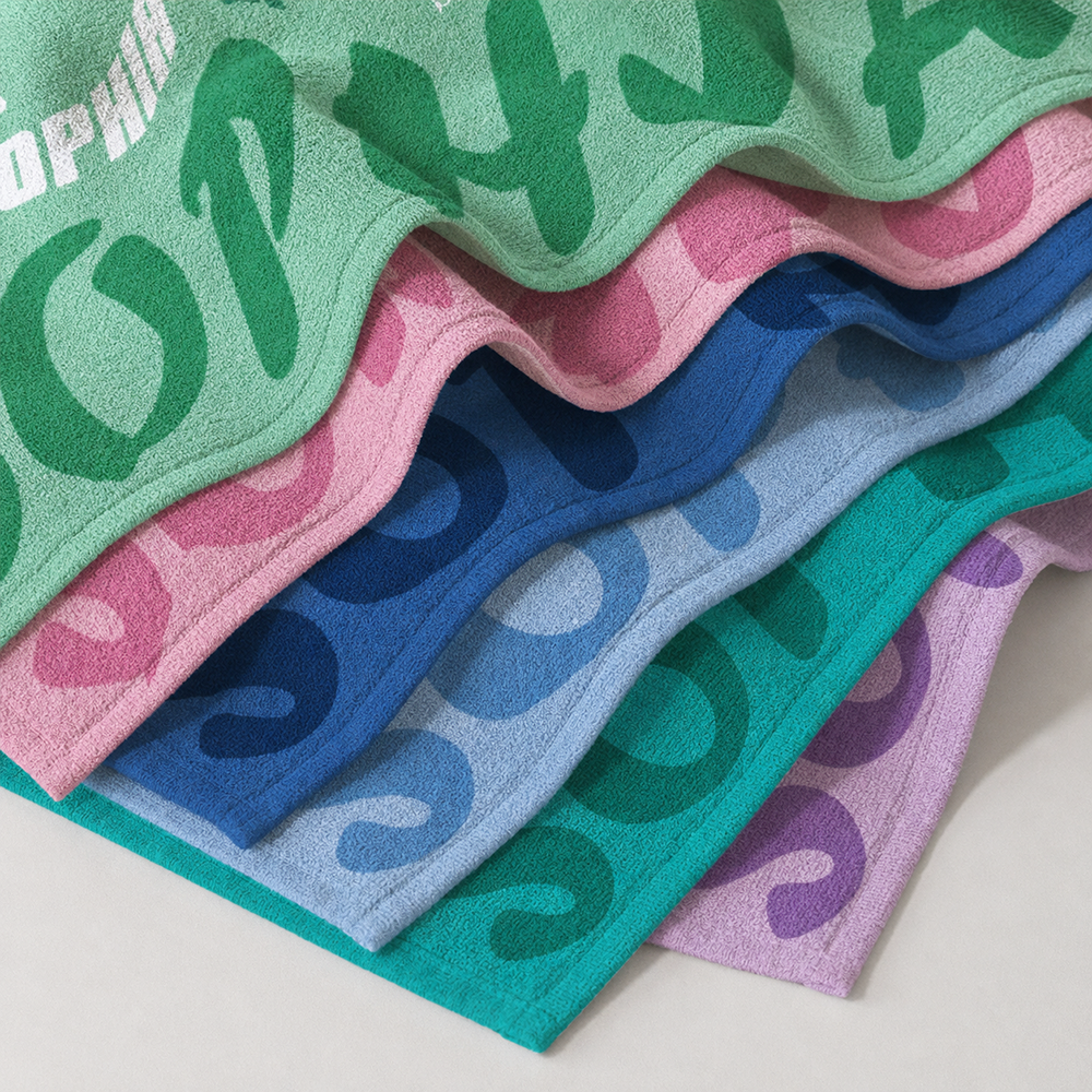 Stacked personalized beach towels in multiple colors showing soft microfiber material and custom initial designs