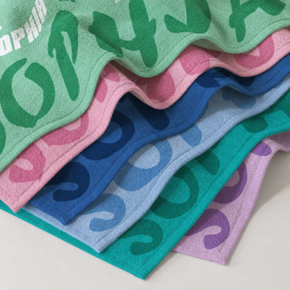 Stacked personalized beach towels in multiple colors showing soft microfiber material and custom initial designs