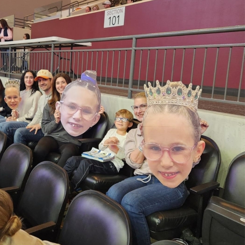 Family at arena seating with kids holding big head cutouts with crowns